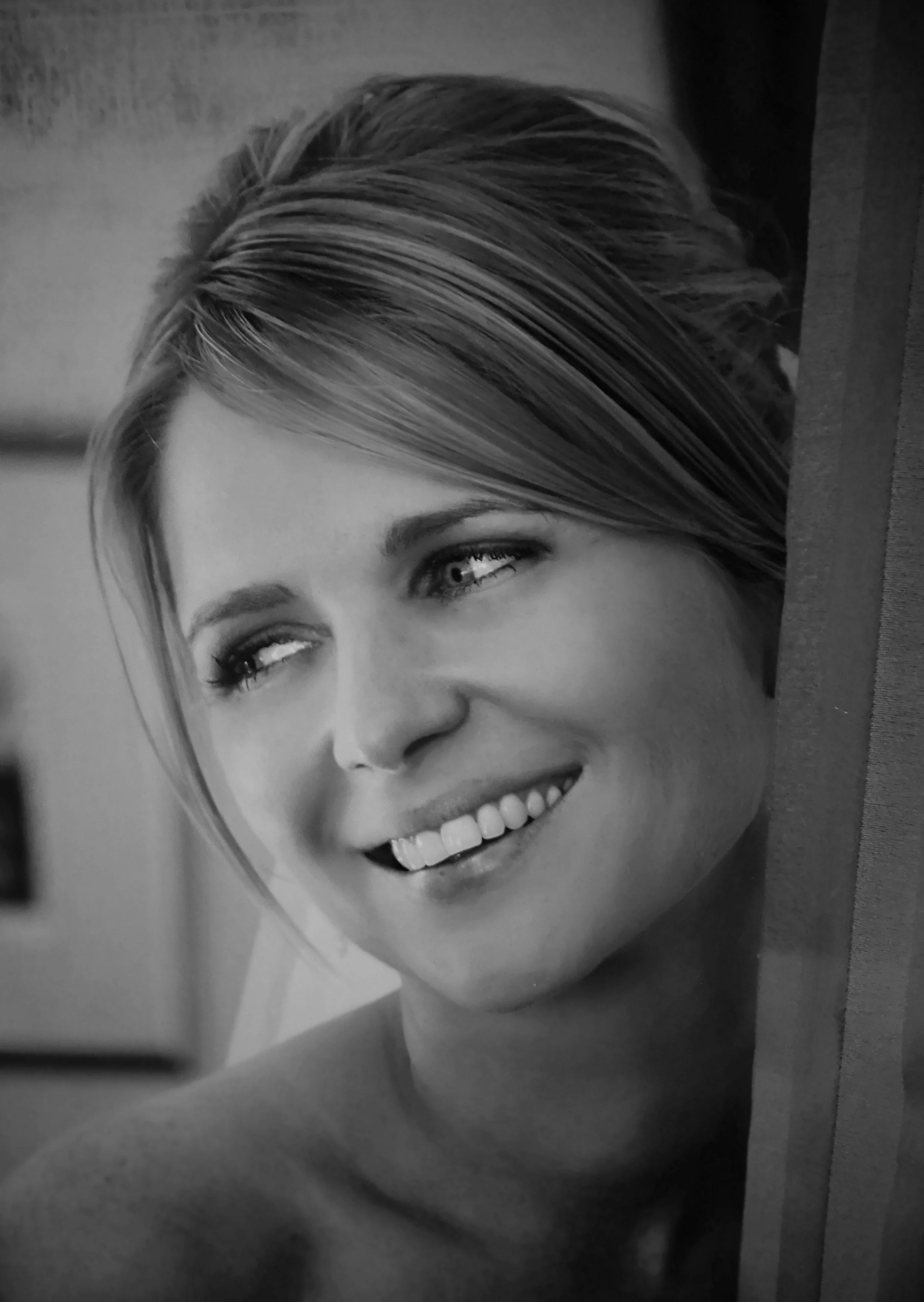 Close-up black and white photograph of a woman with short hair smiling, with her head turned slightly to the side.