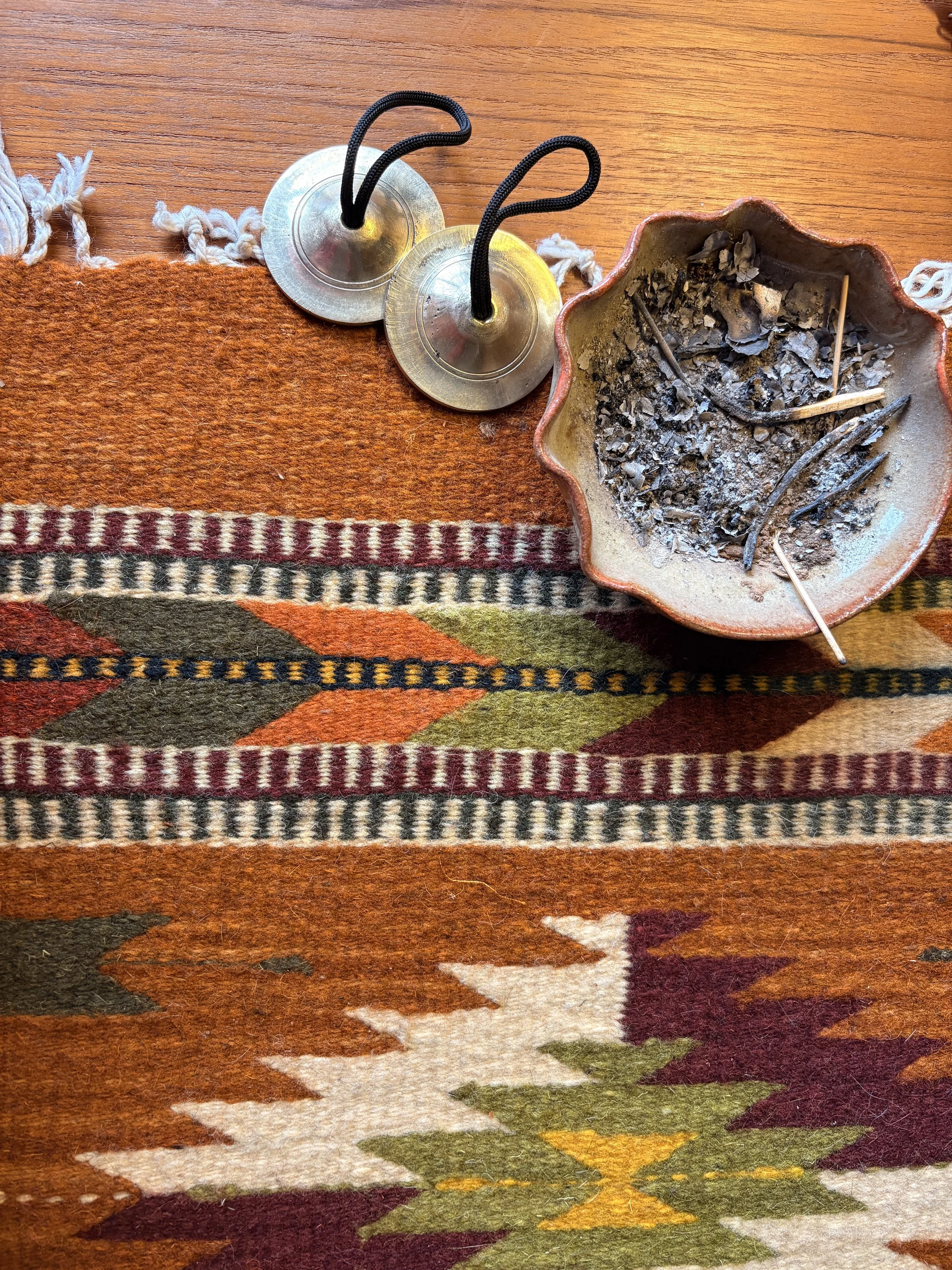 An ashtray filled with ashes and cigarette butts on a colorful patterned rug. Two metal spinning top toys are placed next to the ashtray on a wooden surface.