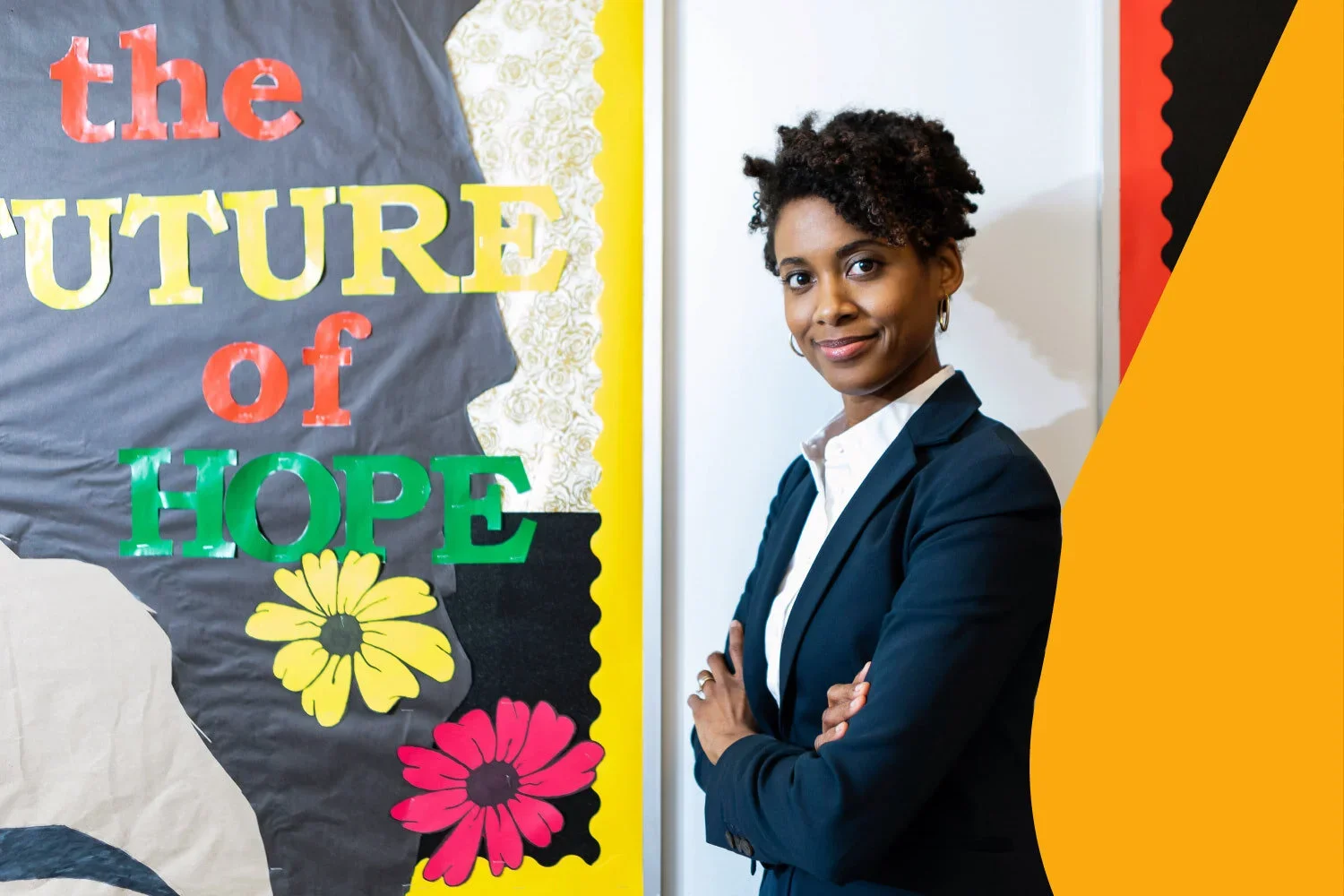A woman in business attire standing with crossed arms in front of a colorful bulletin board with the words "the future of hope" and flower decorations.