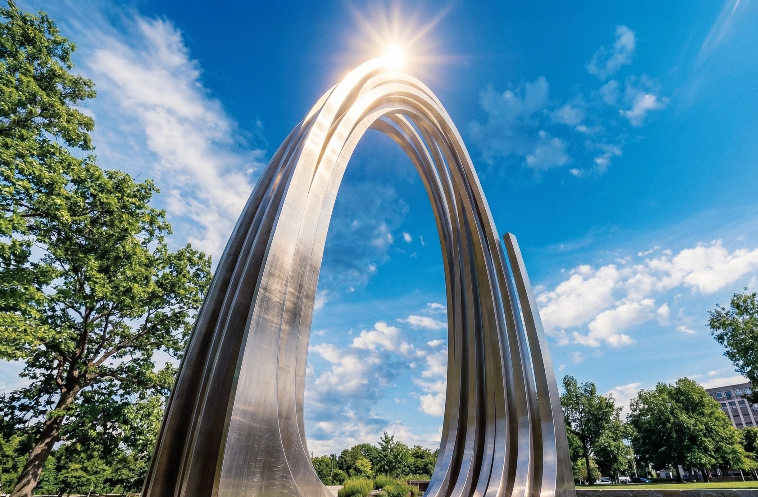 Large metallic sculpture in an outdoor park with green trees and a blue sky with clouds.