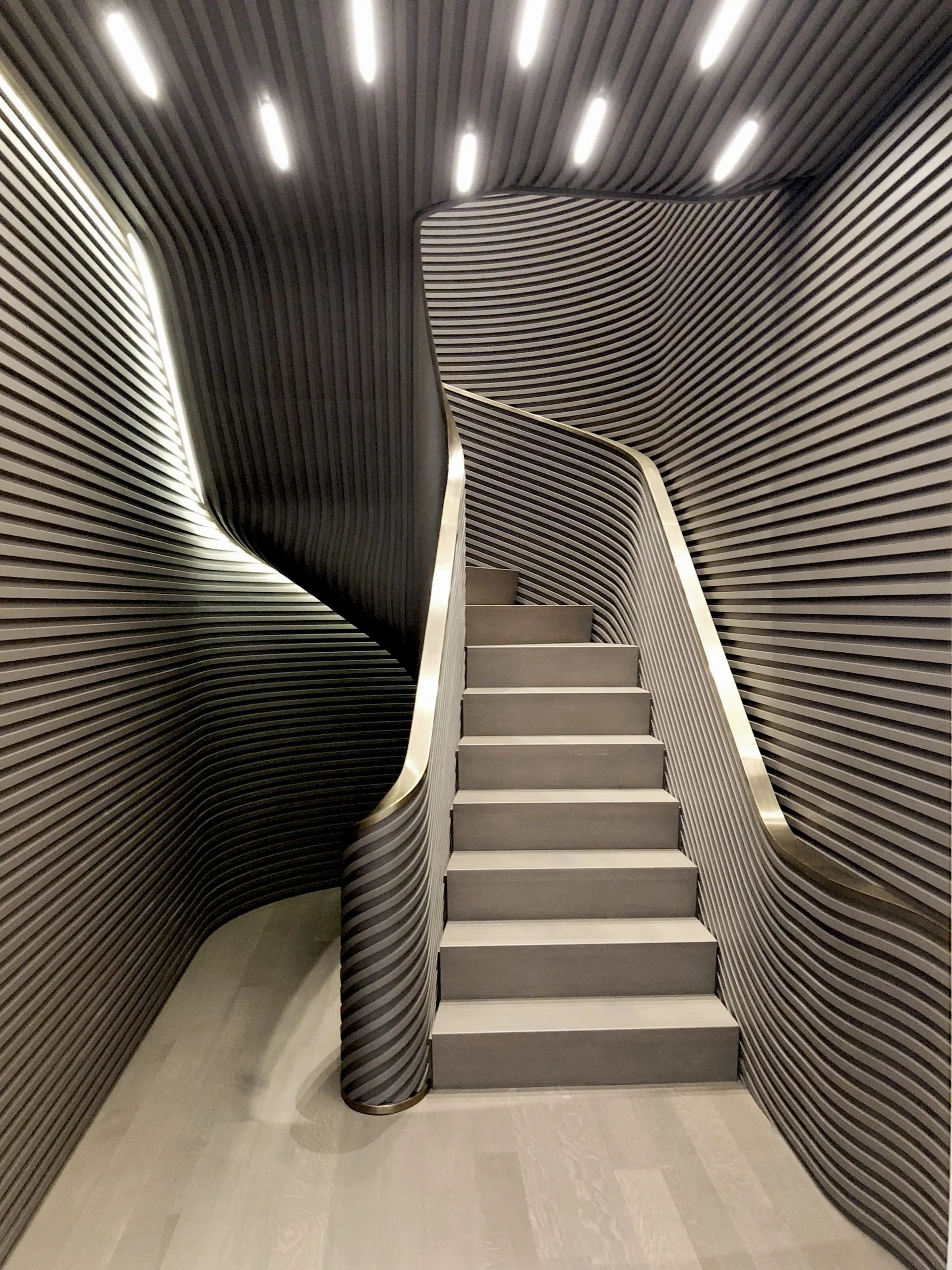 Modern staircase with dark ribbed walls and ceiling, stainless steel handrails, and steps with wooden treads, situated in a sleek, contemporary space.