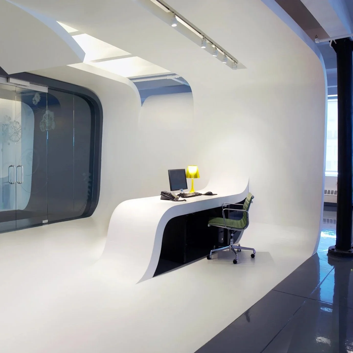 Modern office reception desk with a computer, black phone, yellow lamp, and green chair in a sleek, white, curved design space.