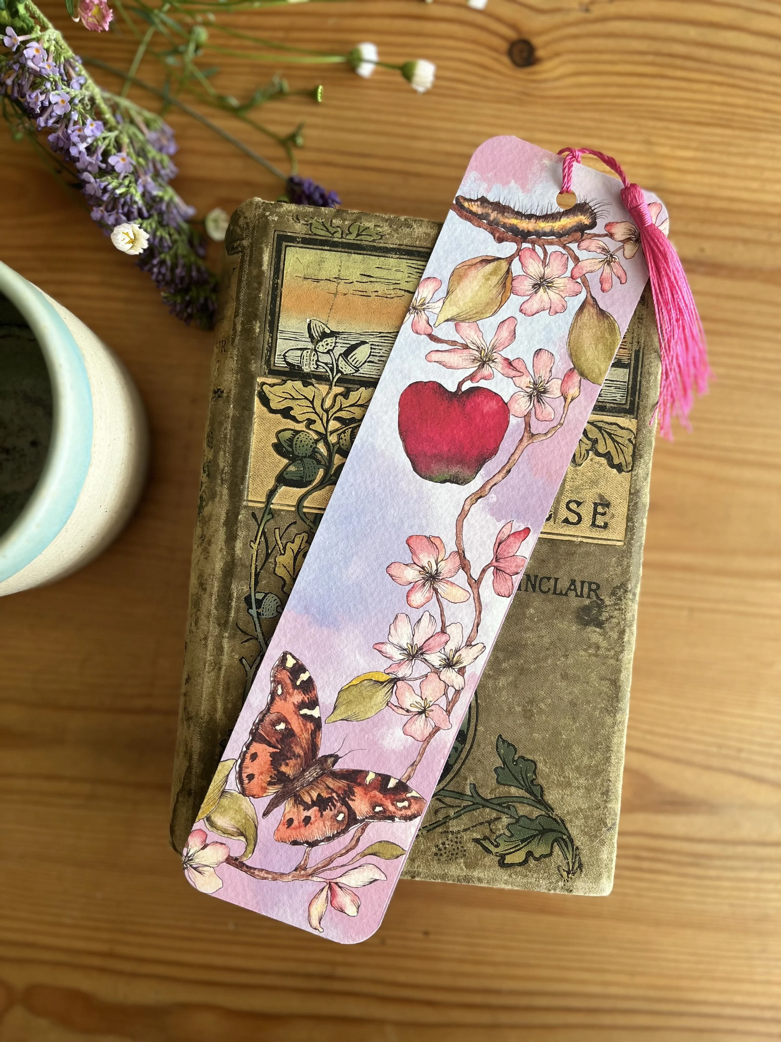 Pale pink bookmark with tassel photographed on a wooden table with tea cup and flowers