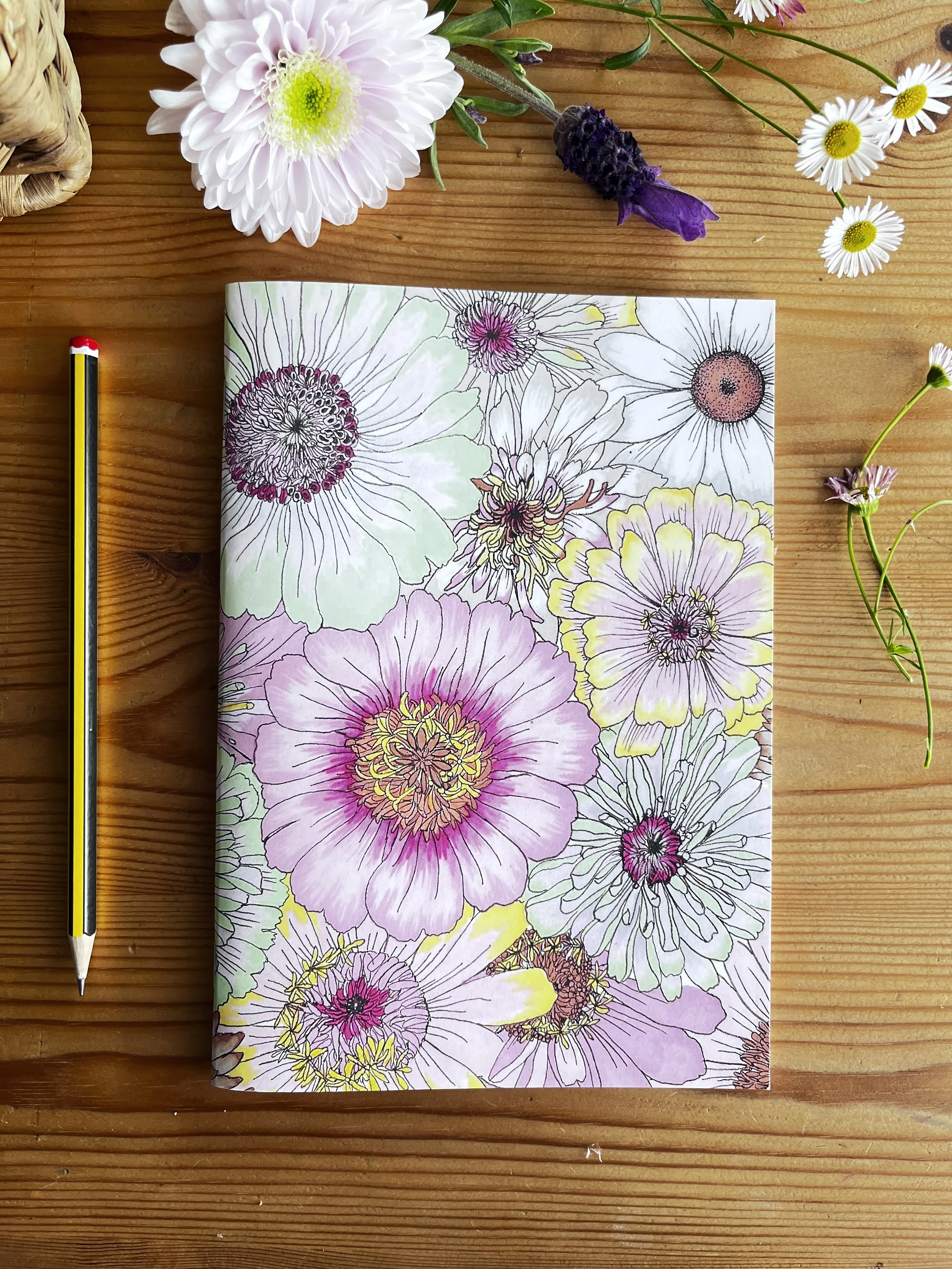 Pale pastel notebook pictured on a wooden table with flowers.