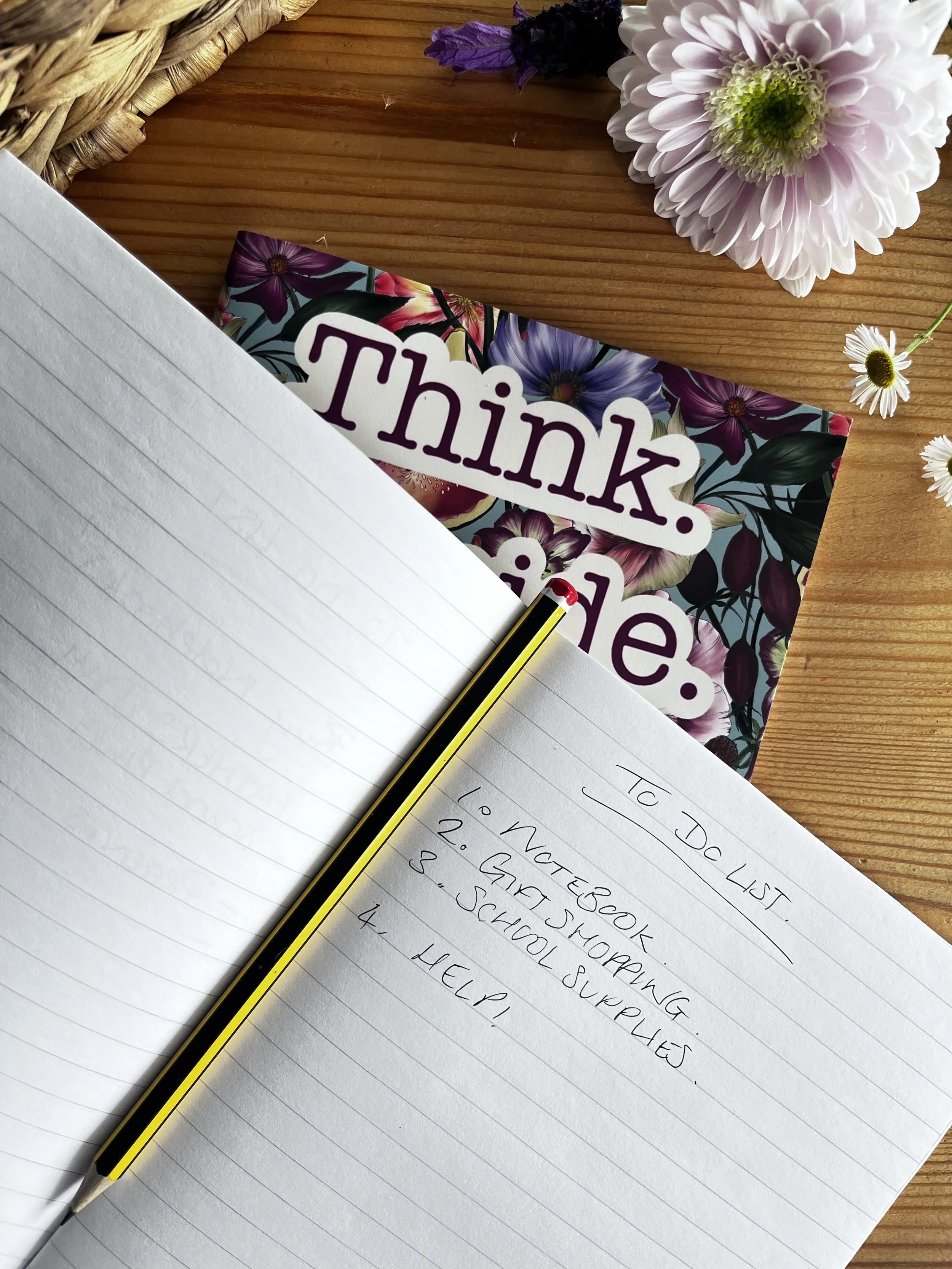 An open notebook pictured on top of a floral patterned notebook with.m a to do list inside of it