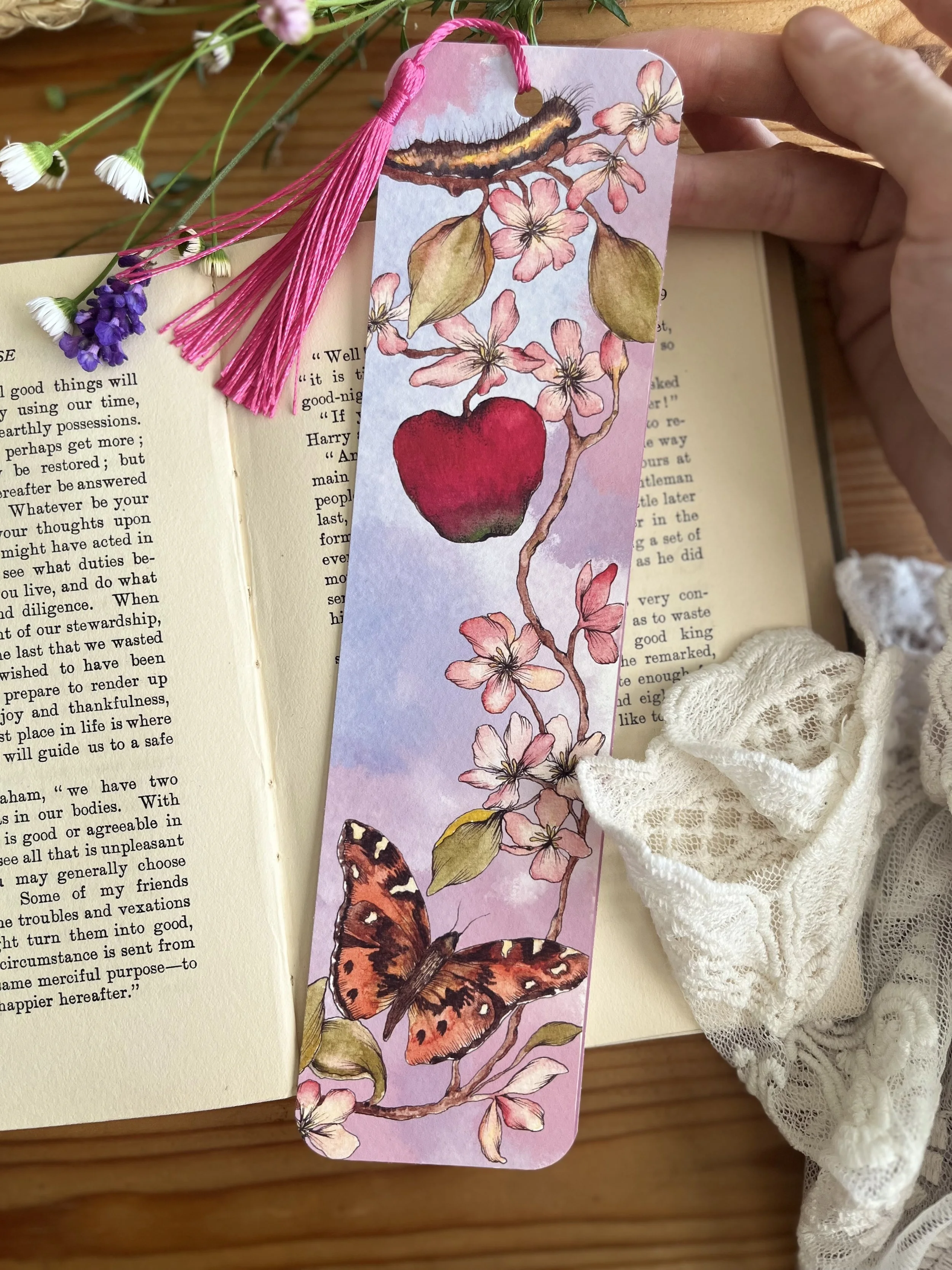 Pale pink bookmark with tassel and flowers. Photographed on an open book with flowers and lace.