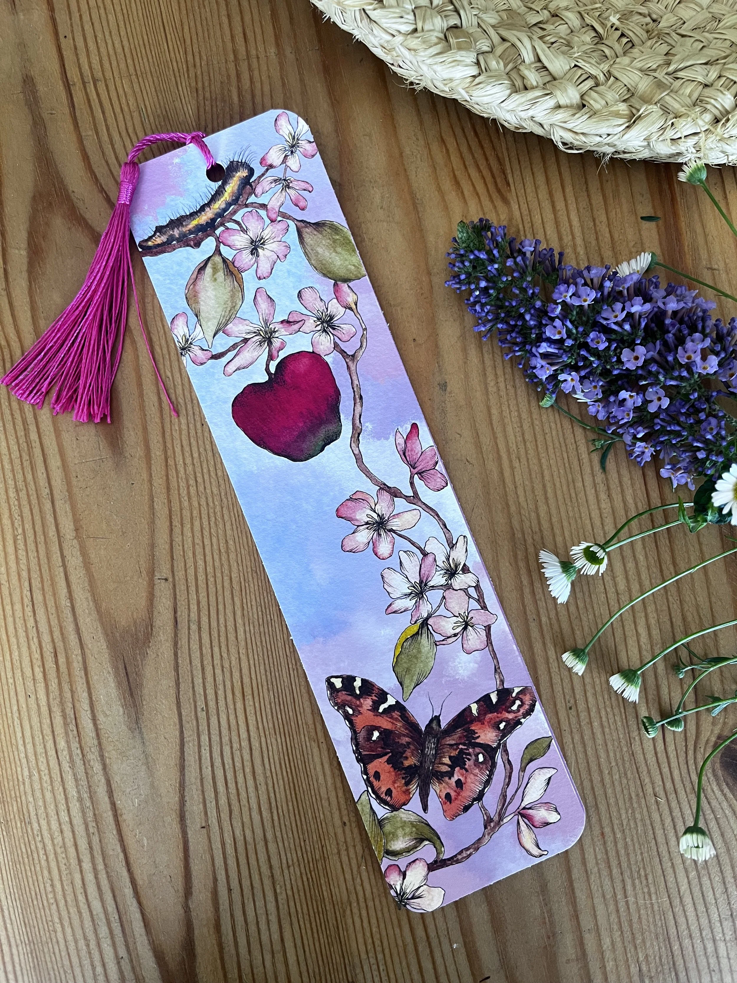 Pale pink bookmark with tassel photographed on a table with the flowers and a straw hat.