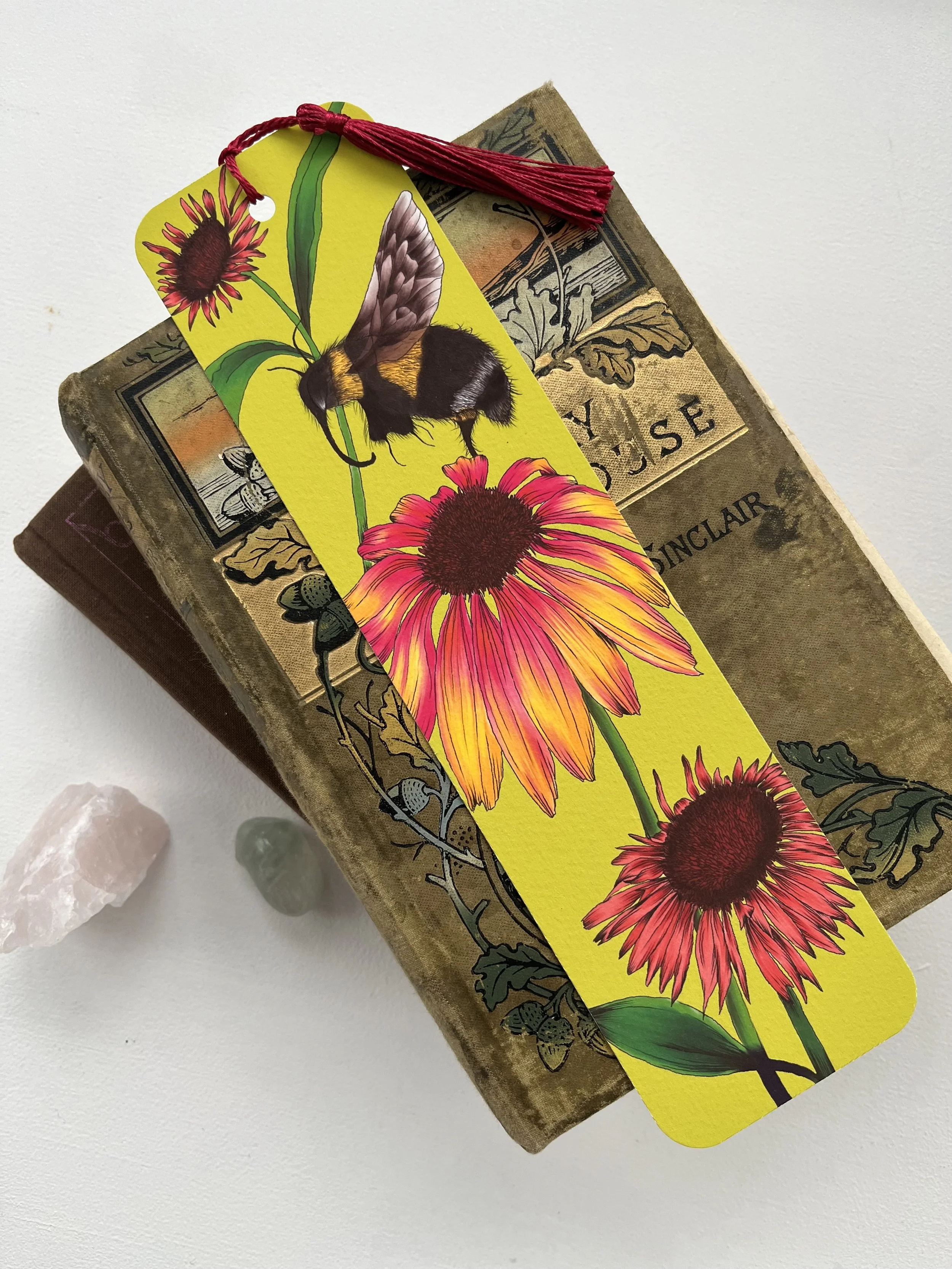 Lime green bookmark with red tassel, the bookmark has a bee and flower design on it. Bookmark photographed on a vintage book.