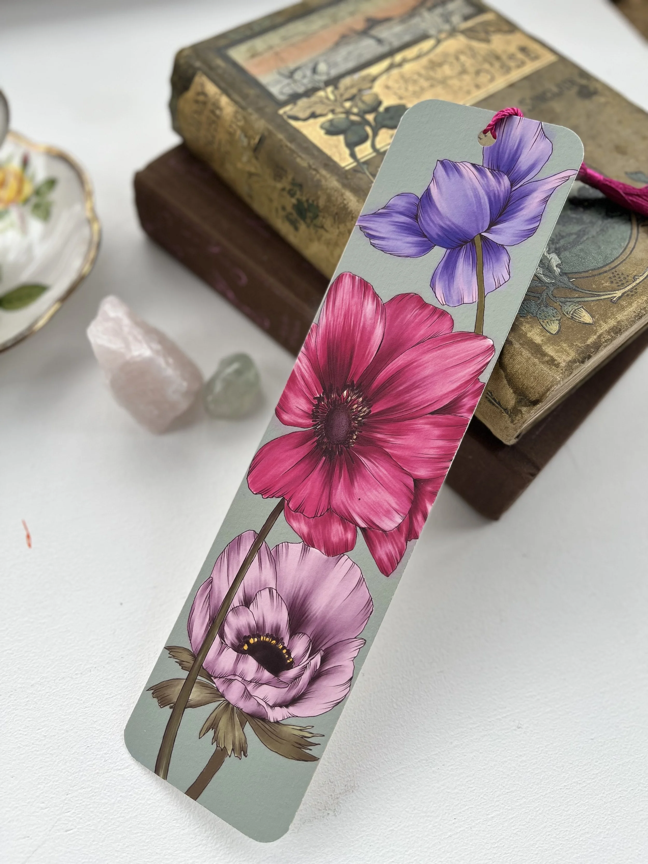A turquoise bookmark with a pink tassel leans against a stack of vintage books.