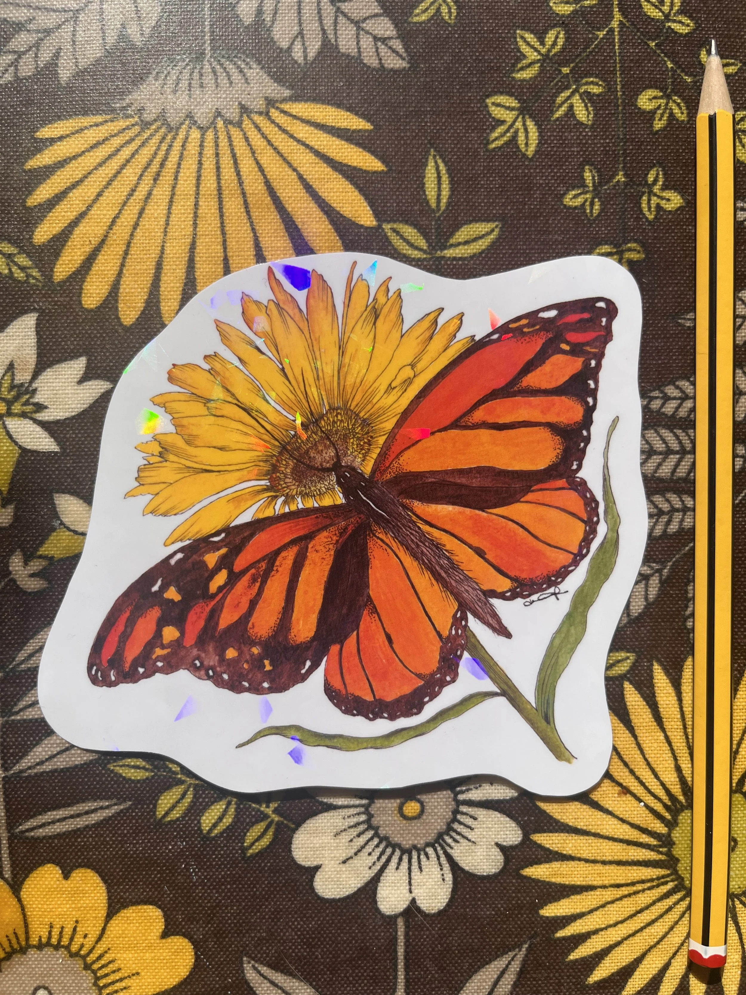 Orange butterfly sticker photographed against a colourful floral tray with a pencil in the background