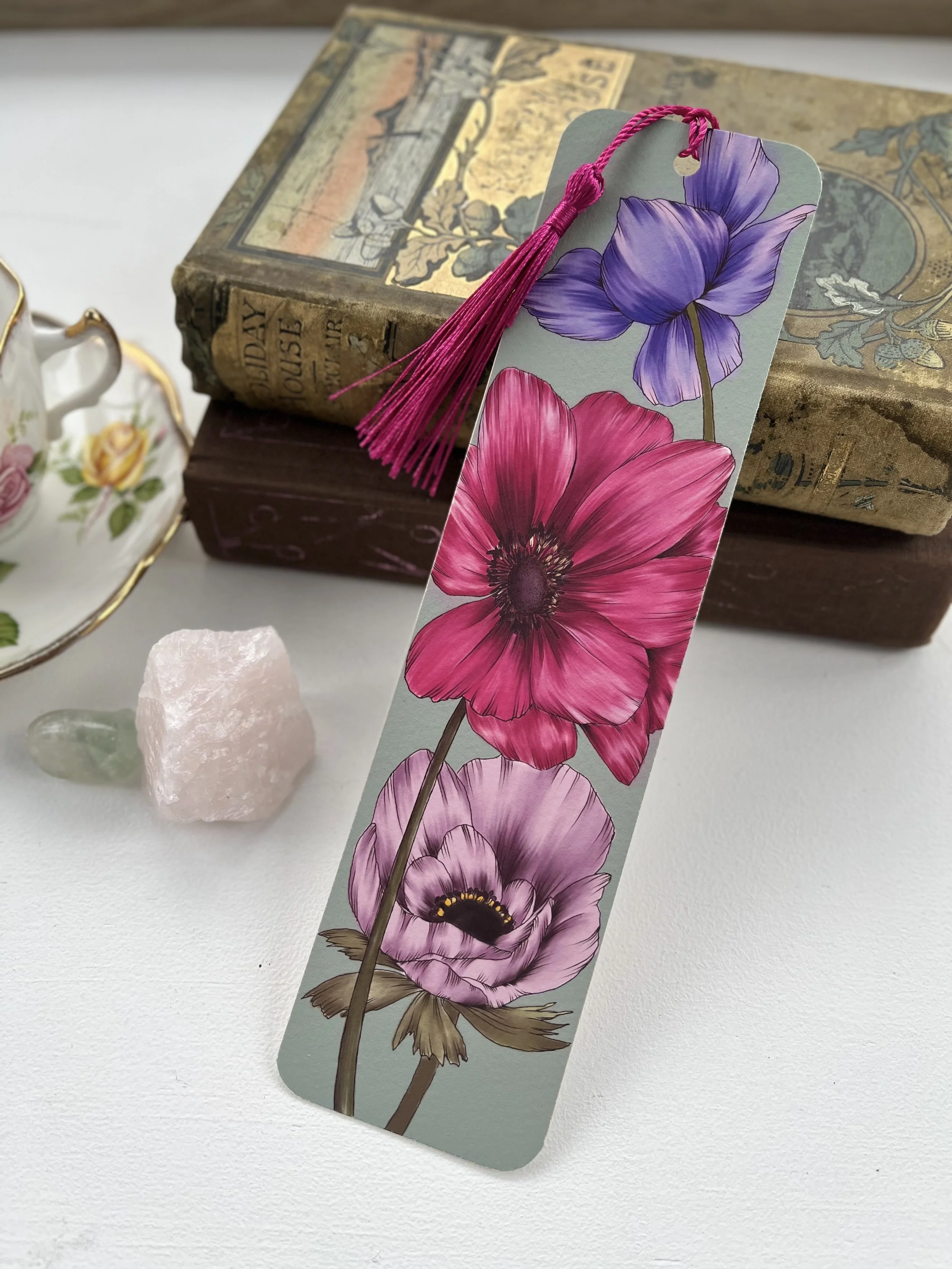 A turquoise bookmark with a pink tassel leans against a stack of vintage books.