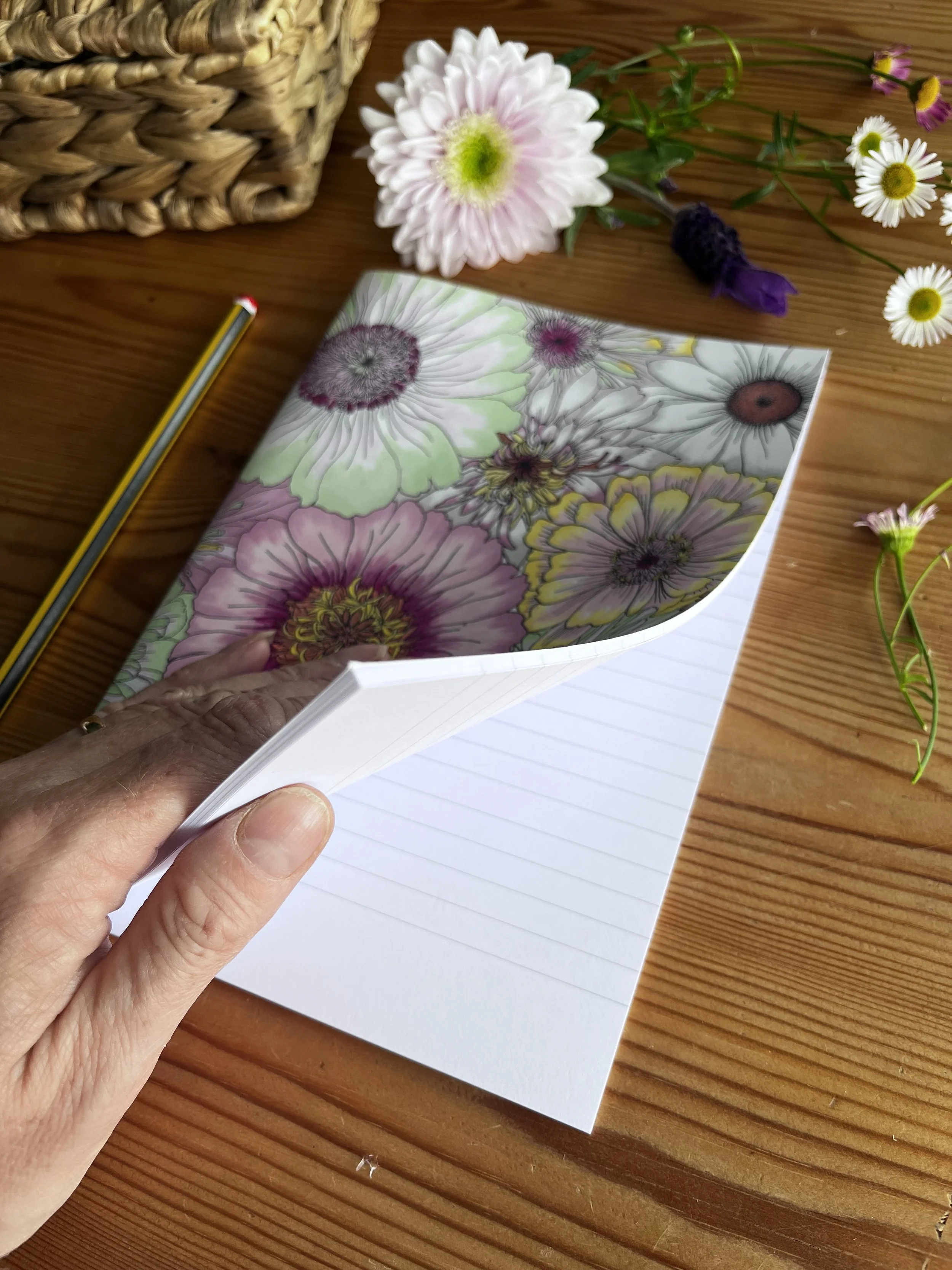 The notebook is  photographed on a wooden table with flowers. A hand holds the notebook open.