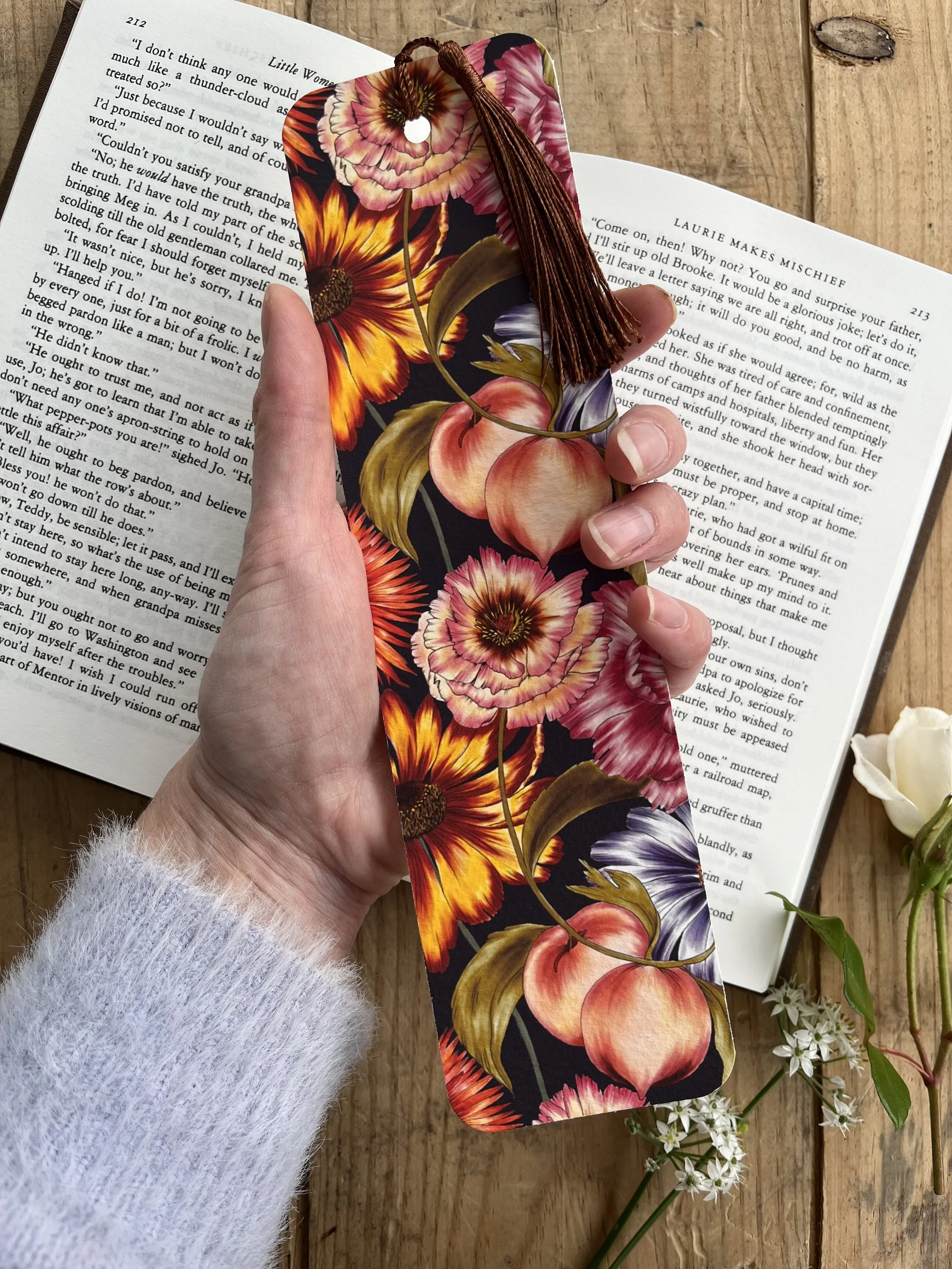 A navy blue bookmark photographed held in a hand with an open book behind