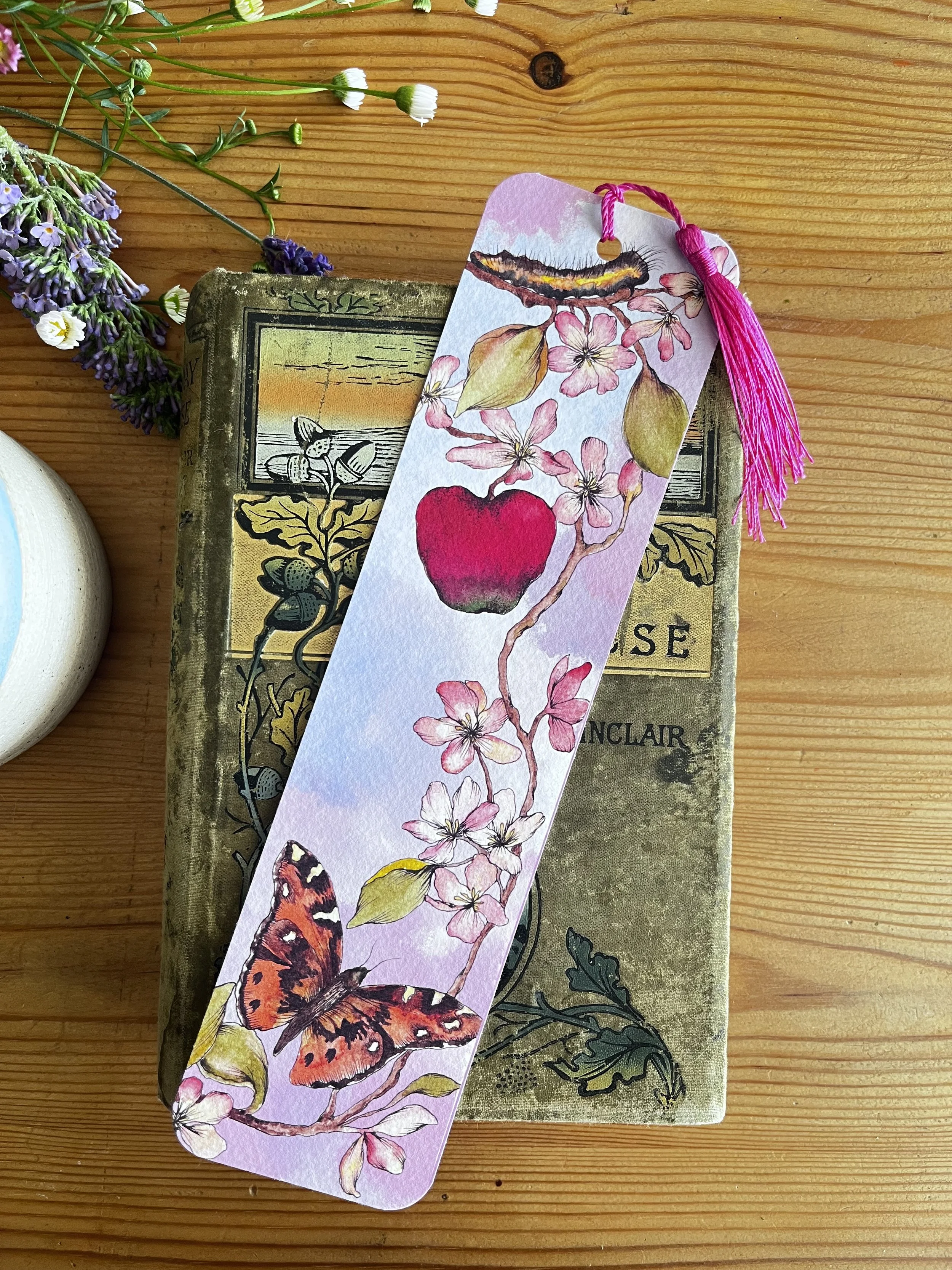 Pale pink bookmark with flowers photographed on a wooden table with a teacup and flowers
