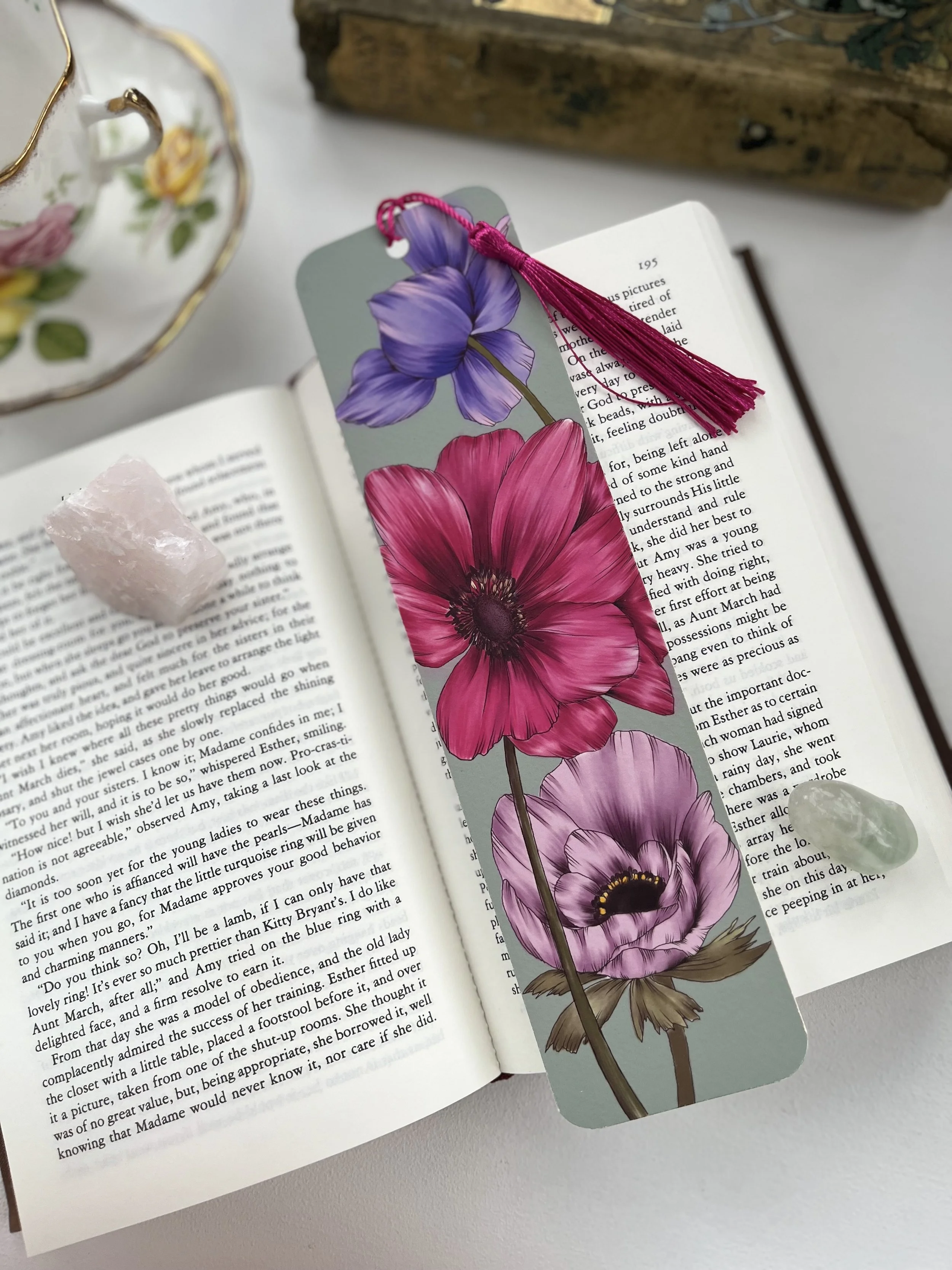A turquoise bookmark with a pink tassel lays on an open books against a white background.