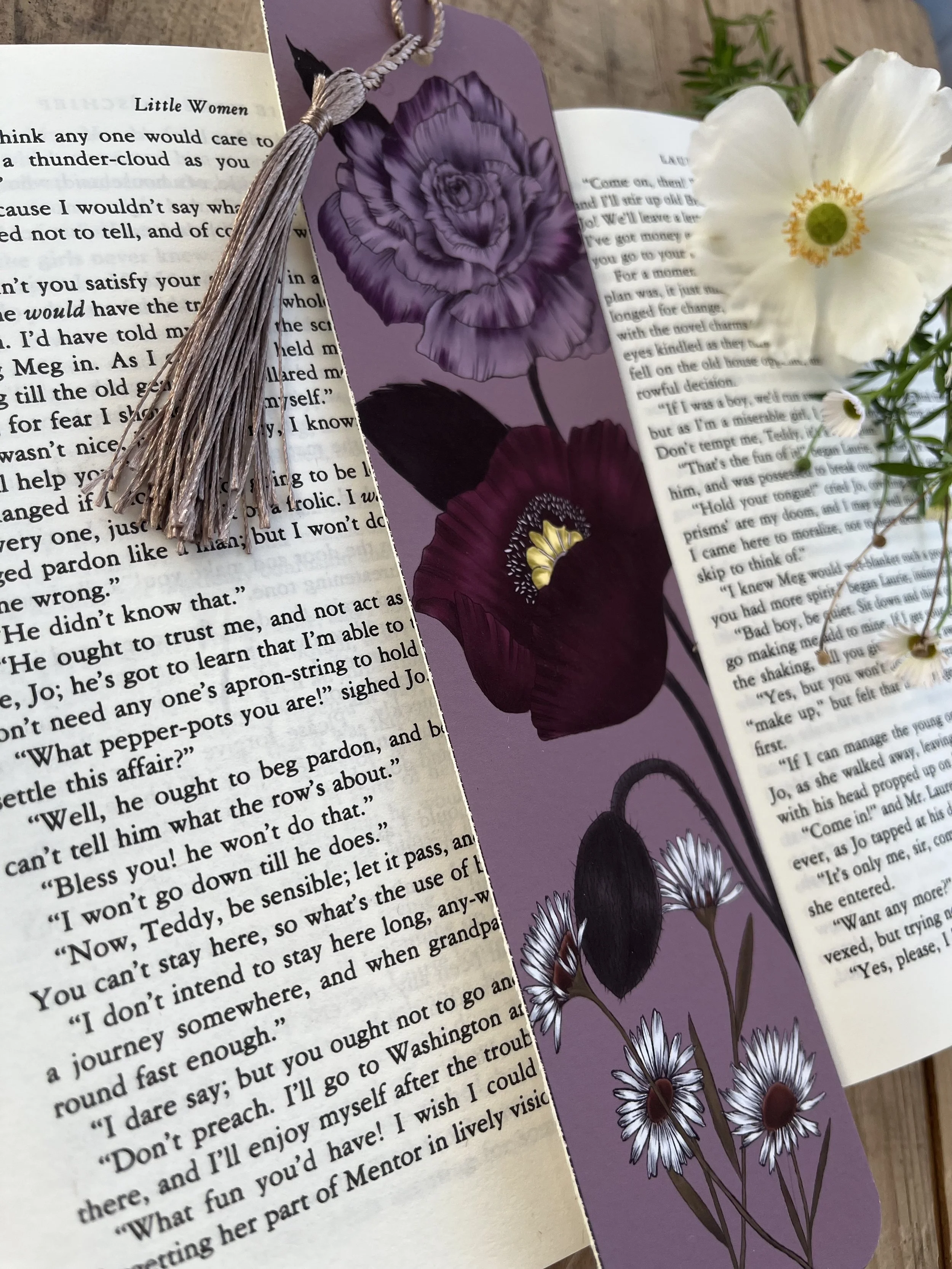 A deep purple bookmark with poppy design and tassel. Photographed on an open book.
