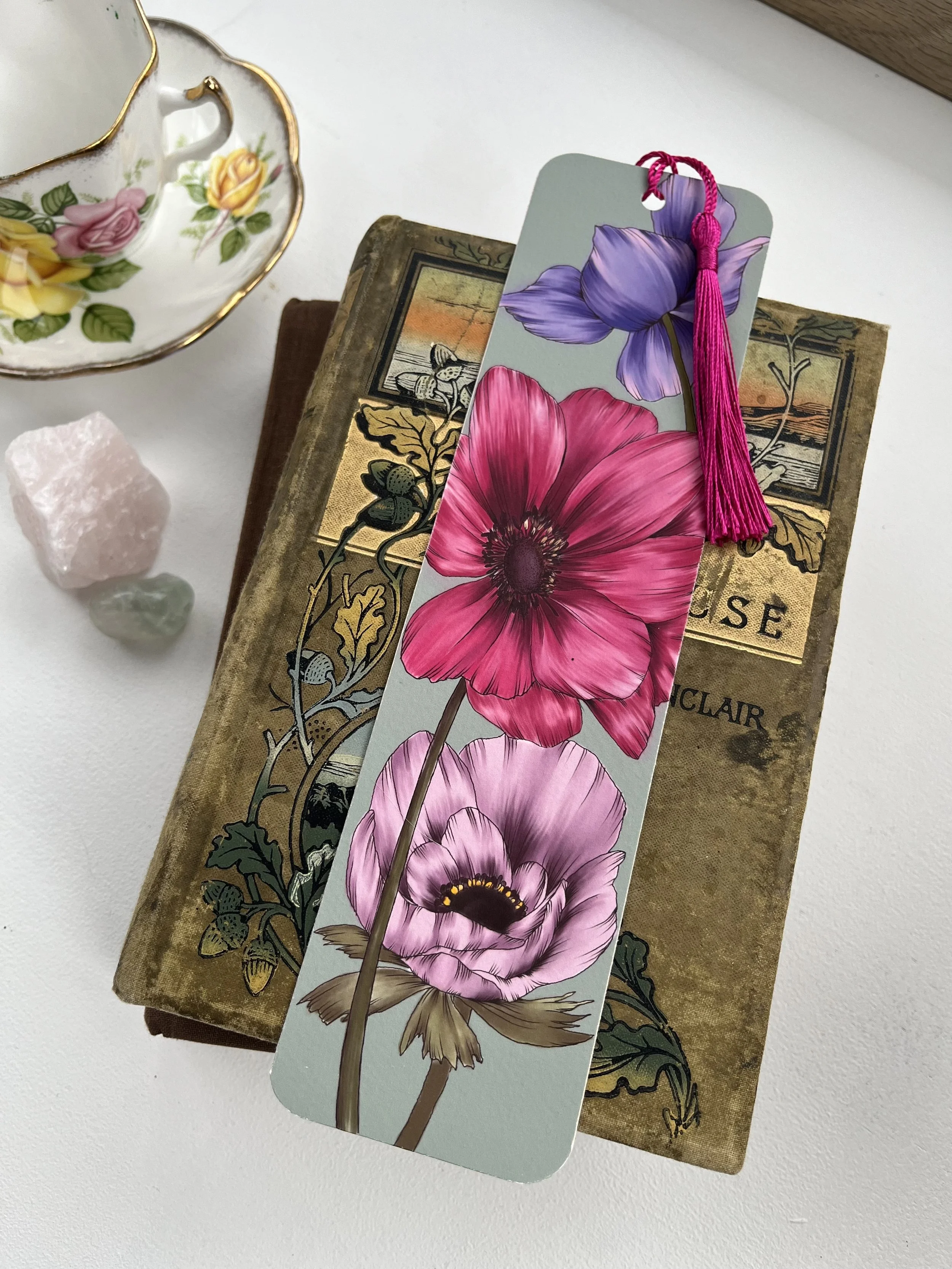 A turquoise bookmark with pink tassel lays across the top of a pile of vintage books