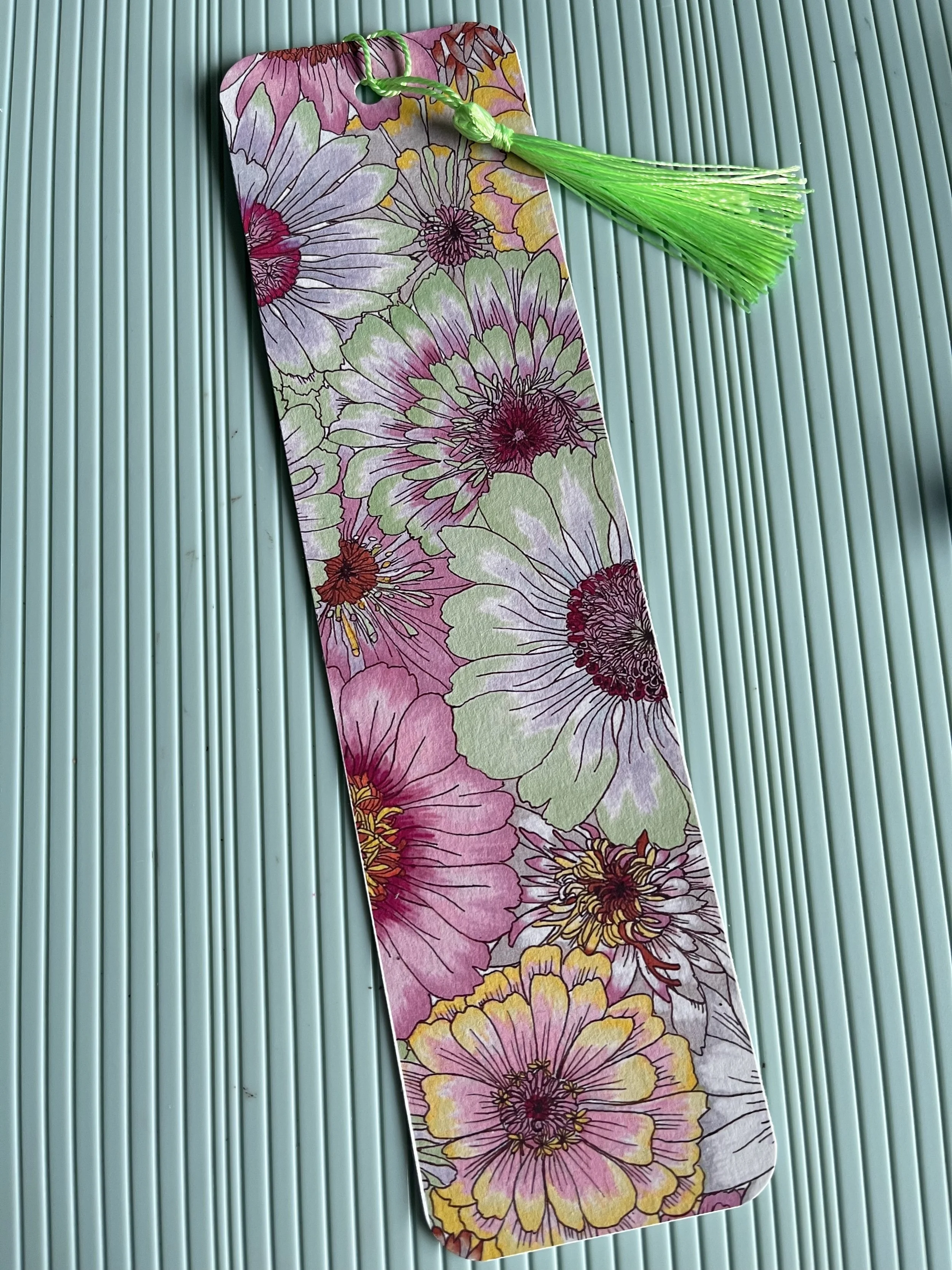 Pastel Daisy bookmark with tassel against a turquoise background.