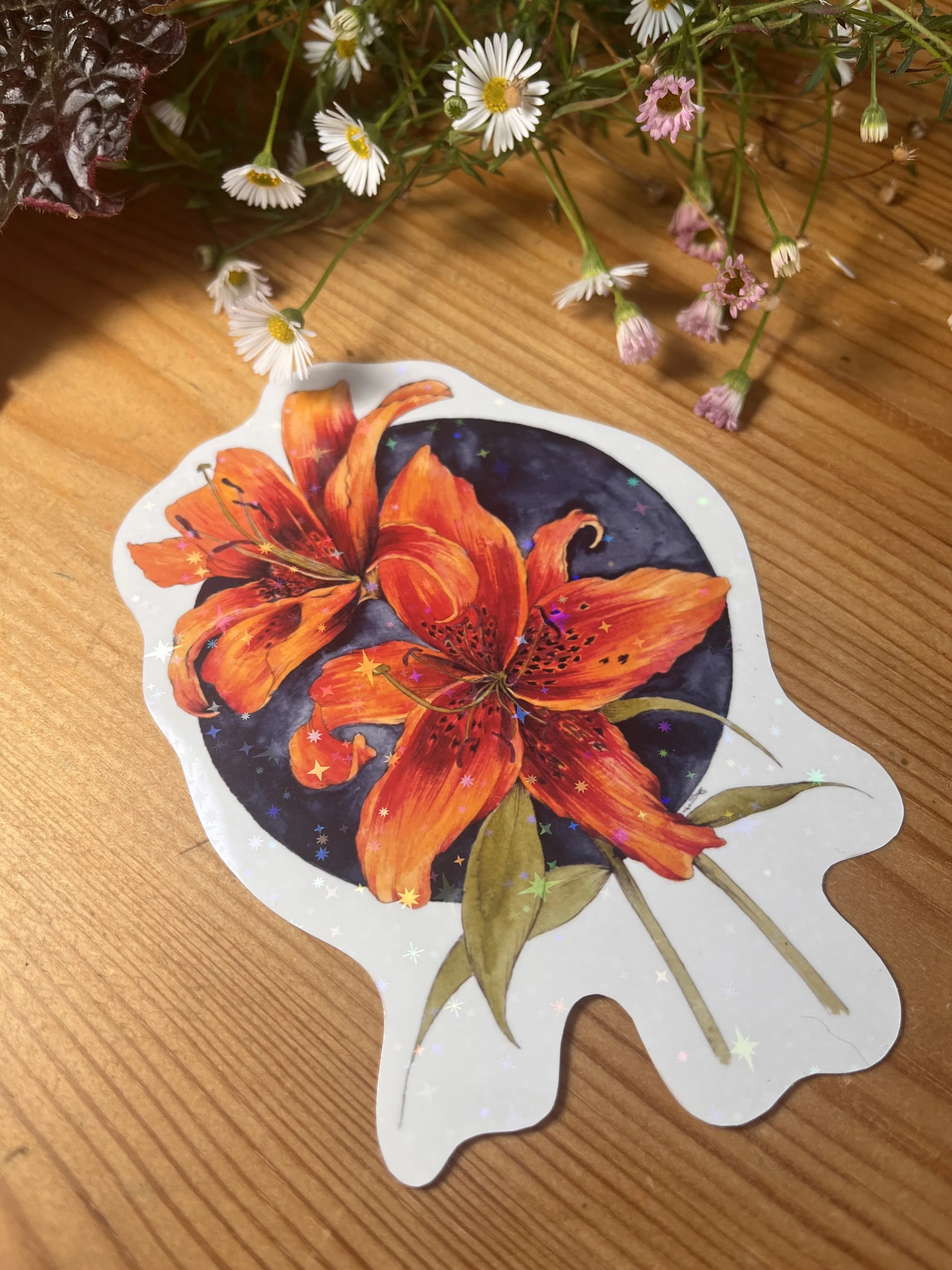 Orange holographic lily sticker photographed on a wooden table with flowers.