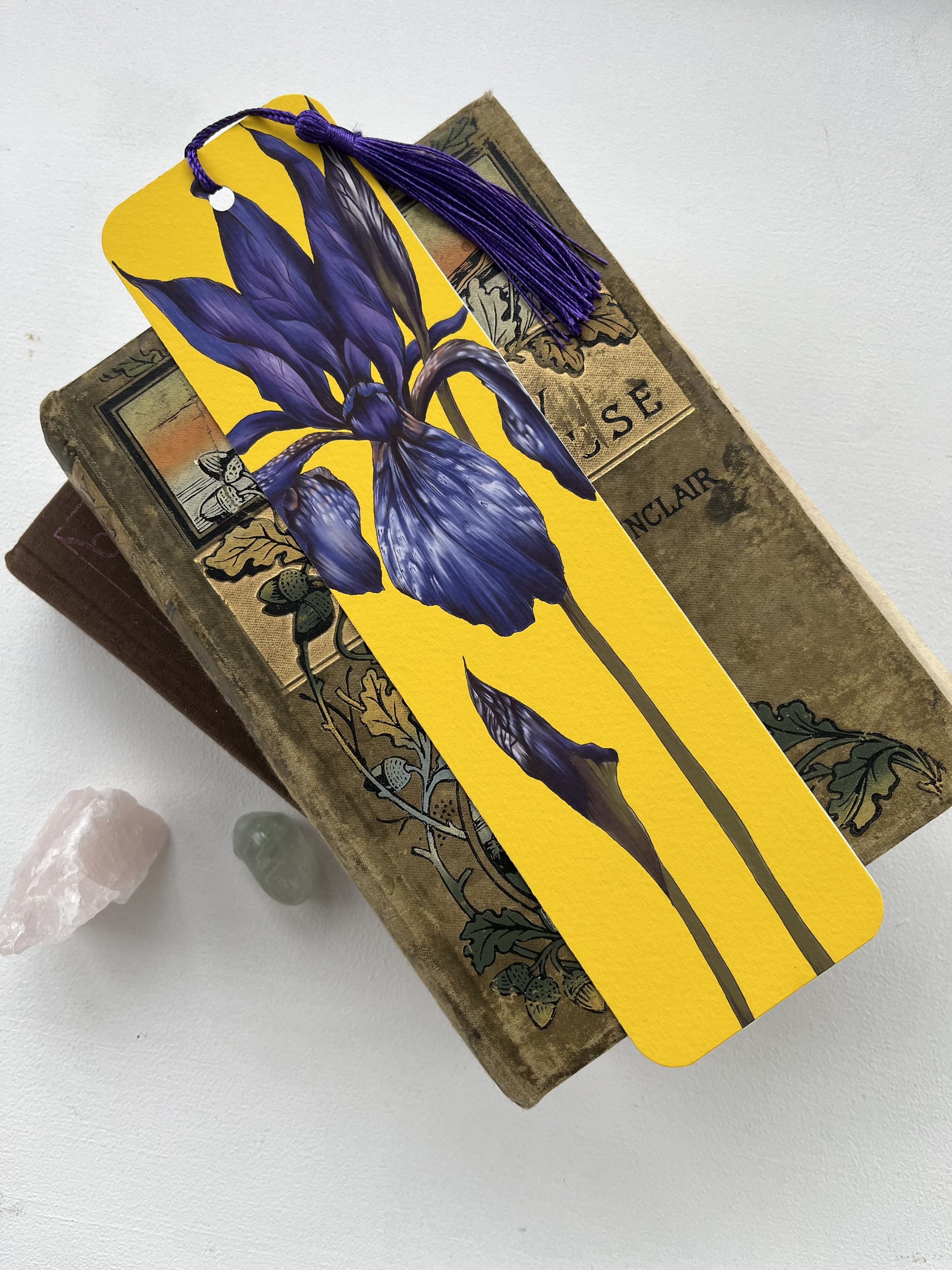 A bright yellow bookmark with purple tassel is pictured laying on the top of a stack of vintage books.