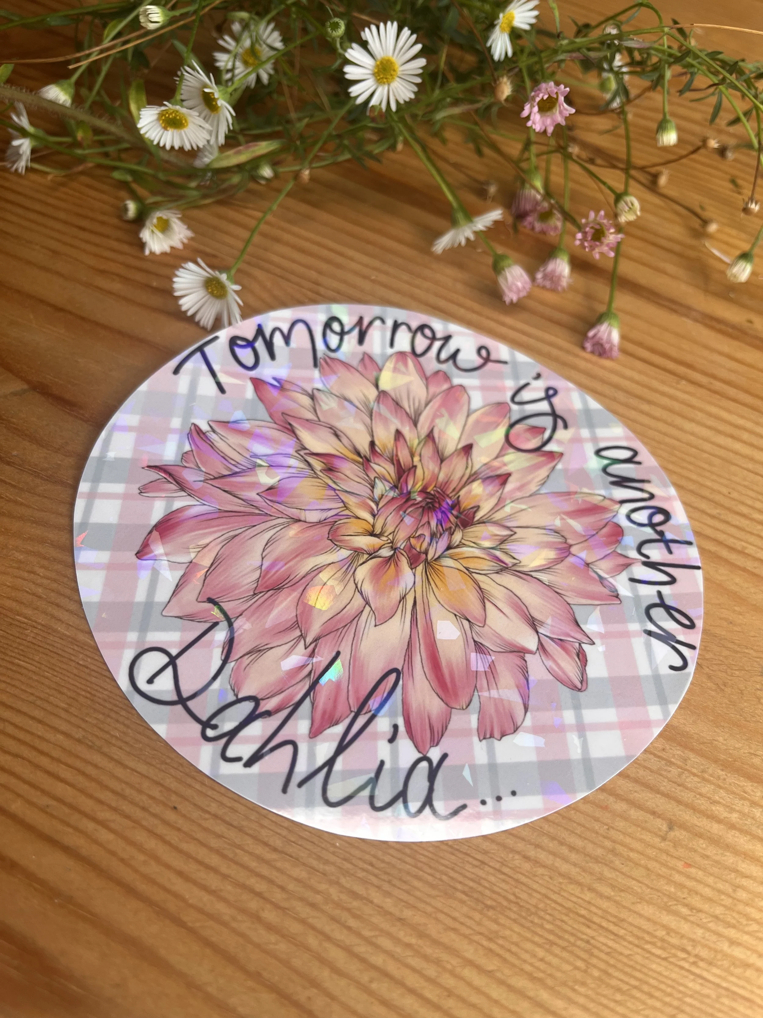 Circular dahlia sticker photographed against a wooden table - the sticker is surrounded by flowers.