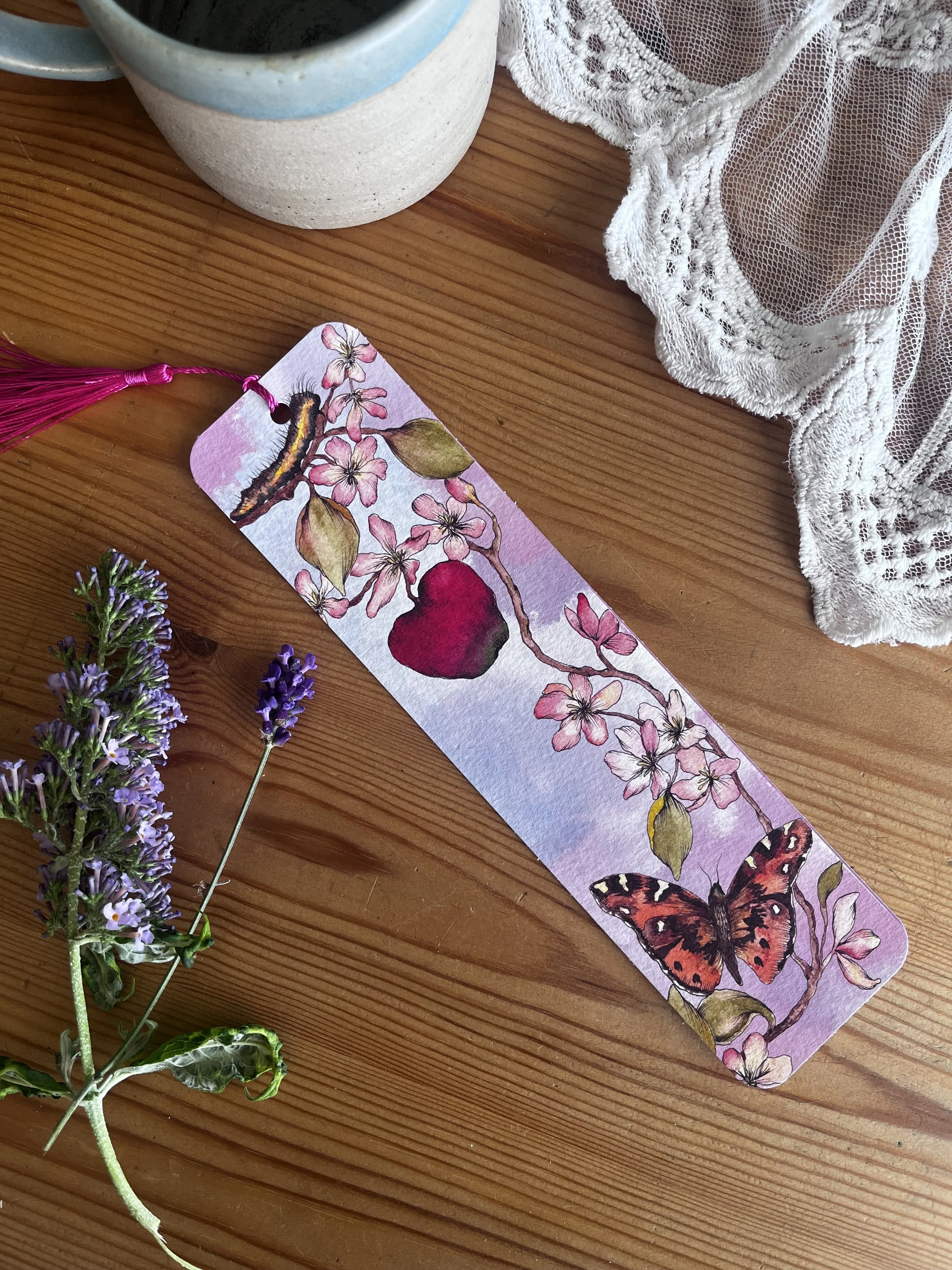 Pale pink flower bookmark with tasel photographed on a table with flowers.