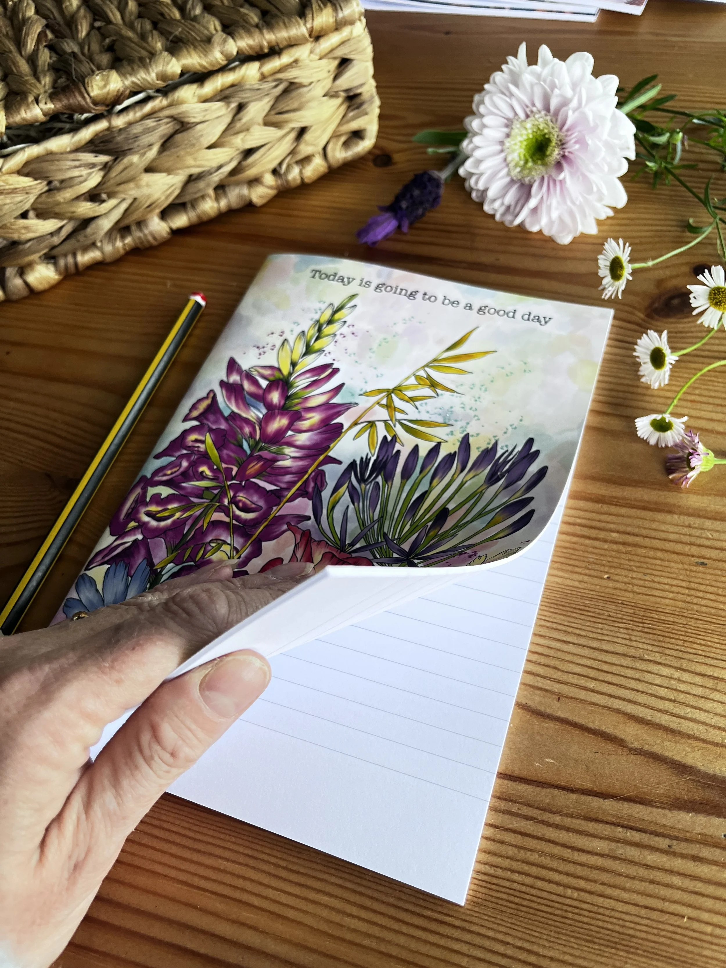 Wildflower notebook photographed being held open by a hand. Photographed with lavender and pale pink chrysanthemum.