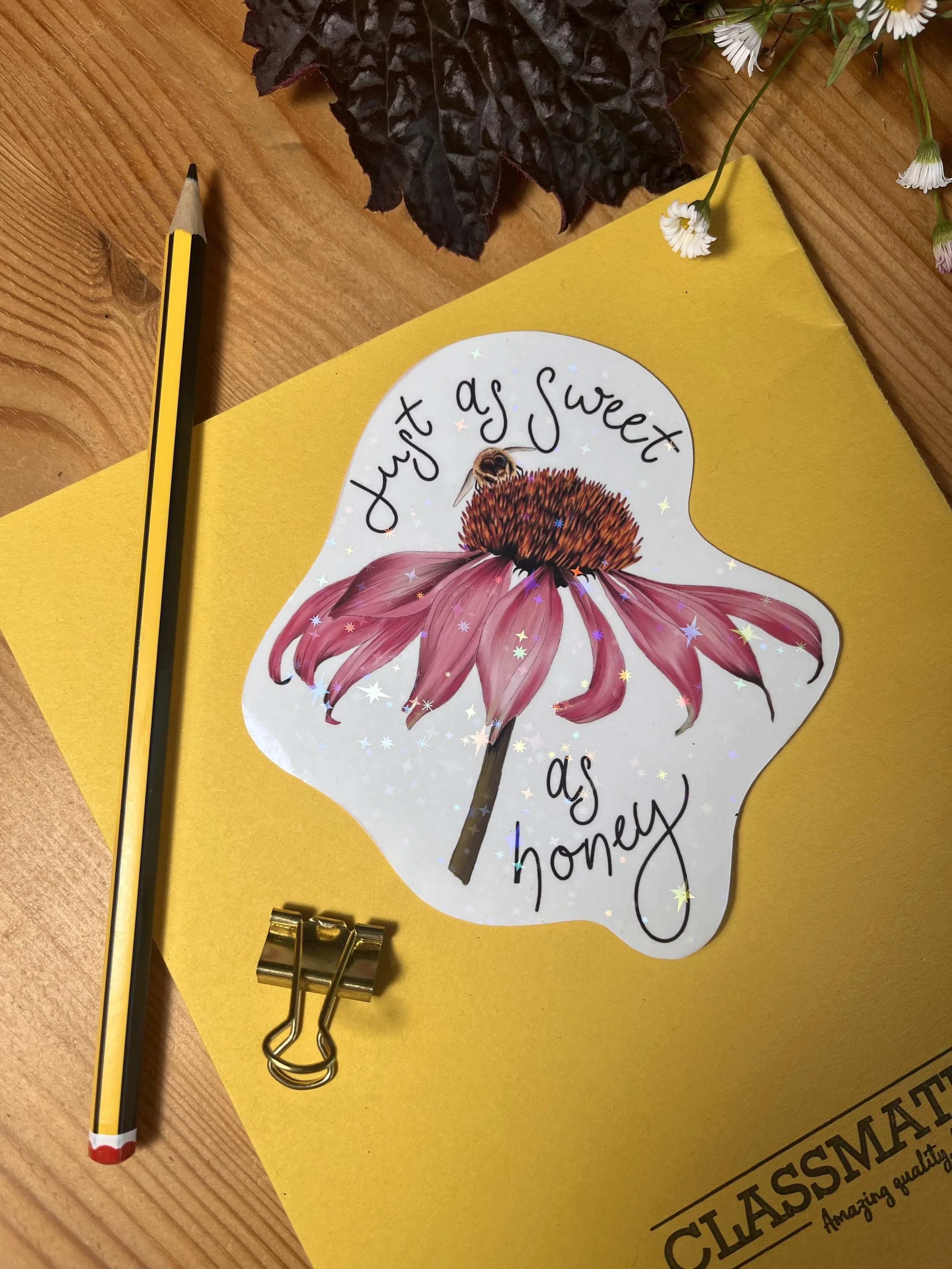 Pink echinacea vinyl sticker photographed front facing against a yellow exercise book and a pencil in the background.