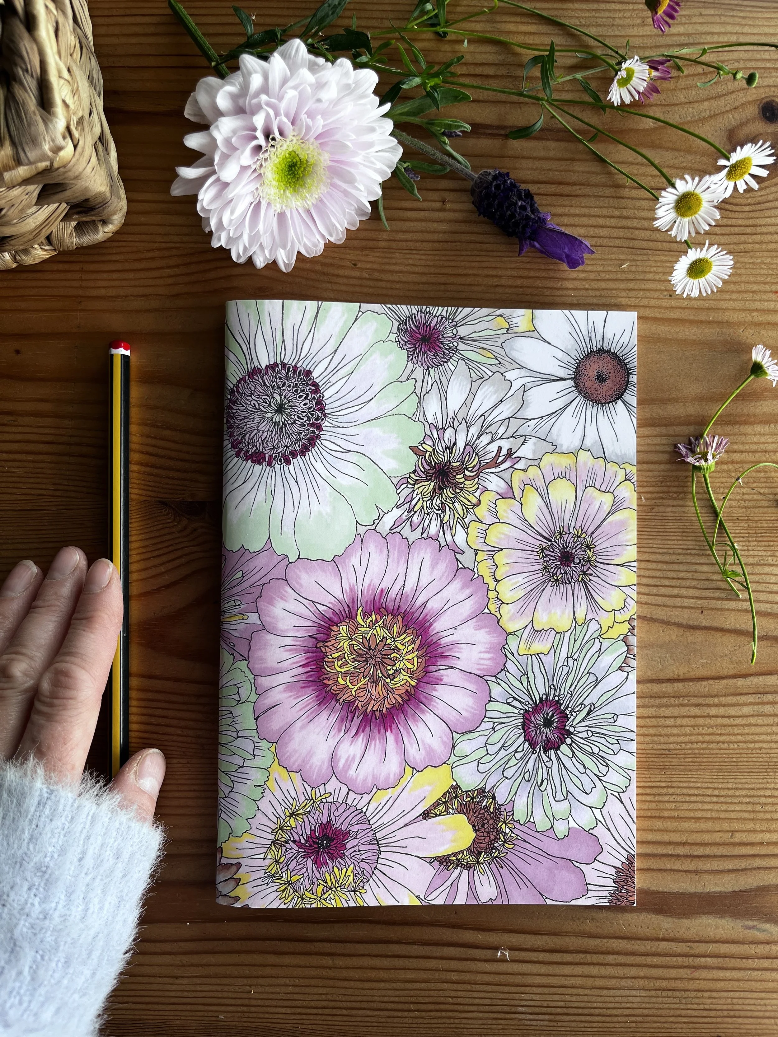 Notebook pictured on a wooden table with Daisy and lavender flowers in the background.