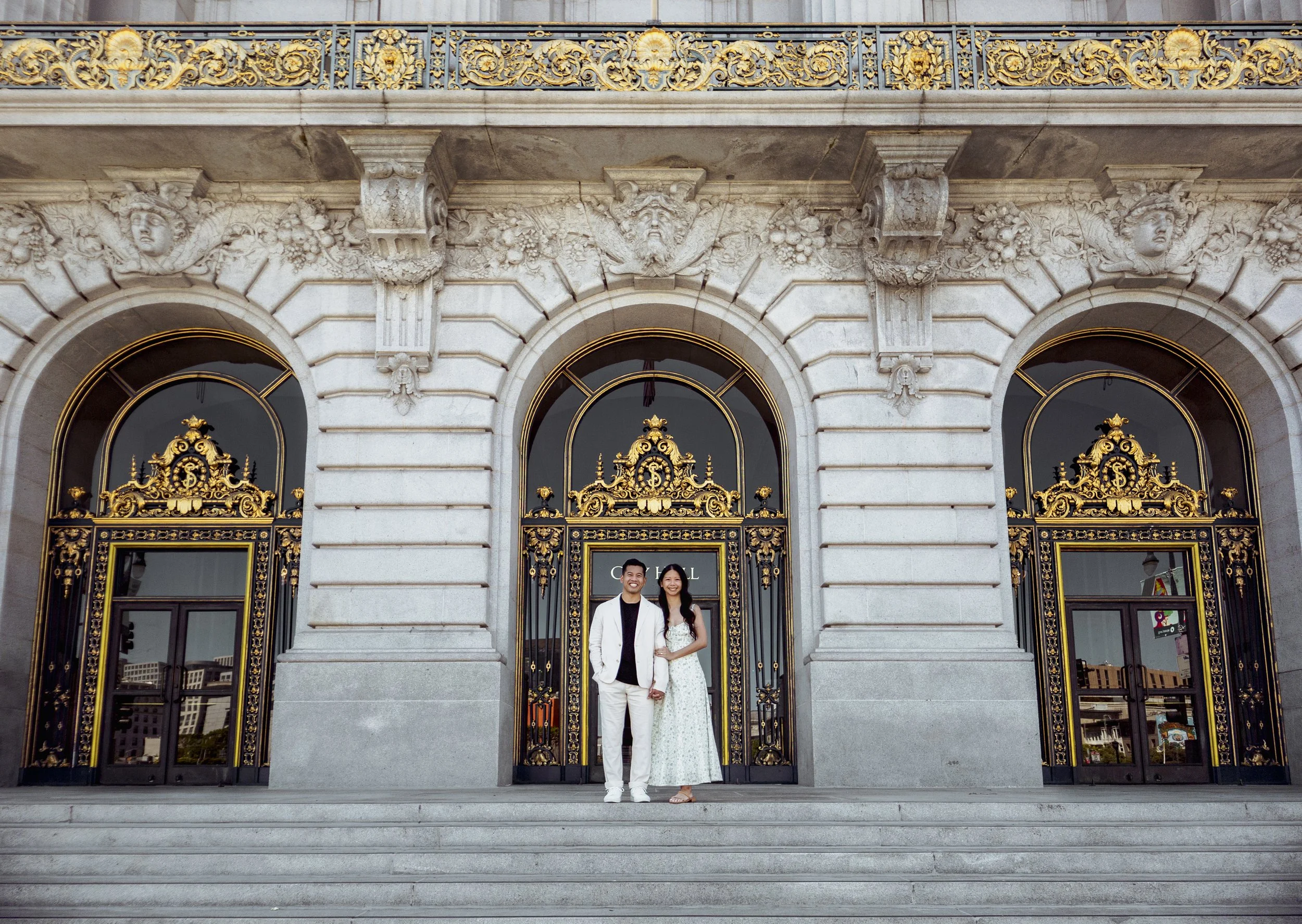 Wide portrait of bride and groom standing together on the steps of San Francisco City Hall.
