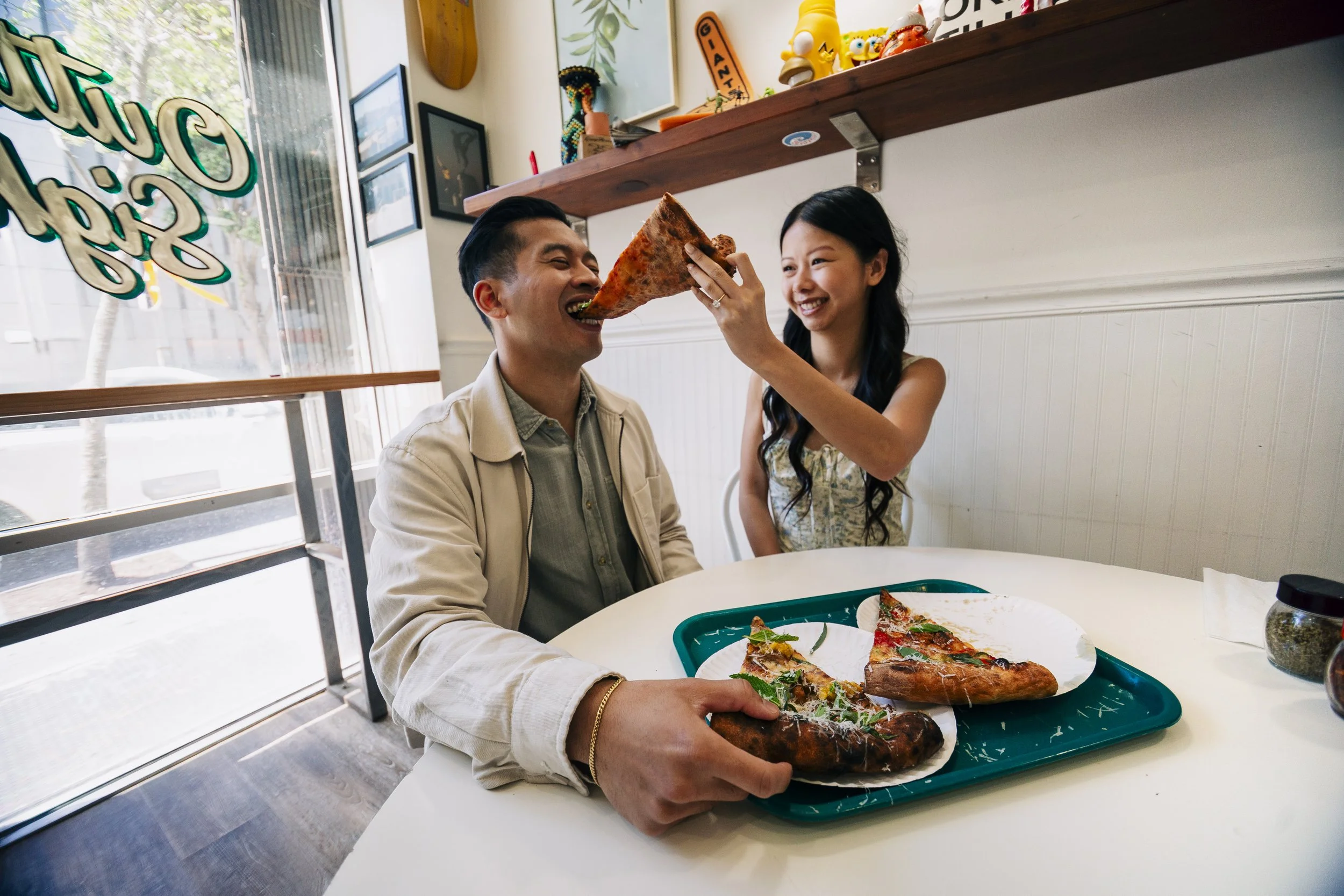 Bride feeding the groom a slice of pizza inside a neighborhood pizza shop in San Francisco.