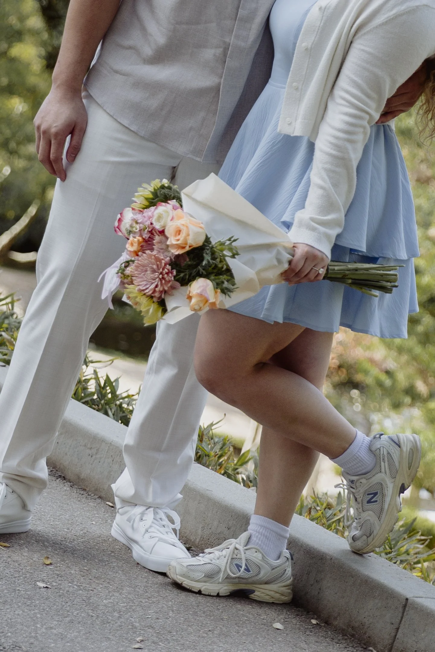Close detail of bride to be holding flowers while embracing her partner.