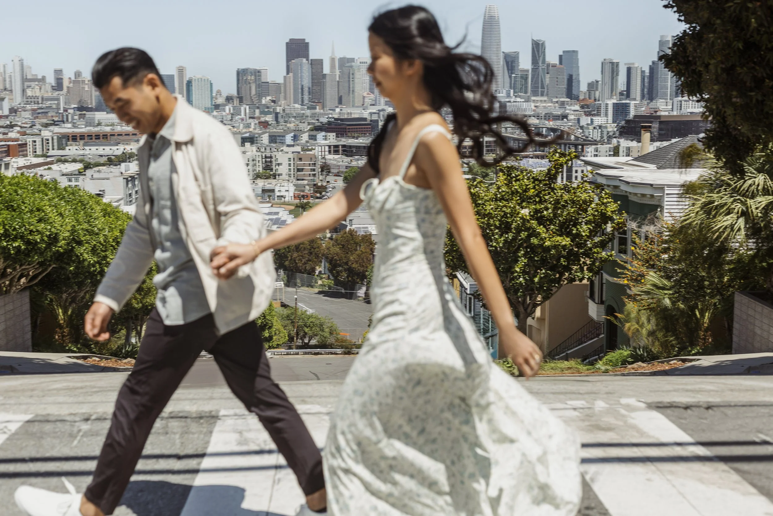 Soft focus image of bride and groom crossing the street with the San Francisco skyline behind them.