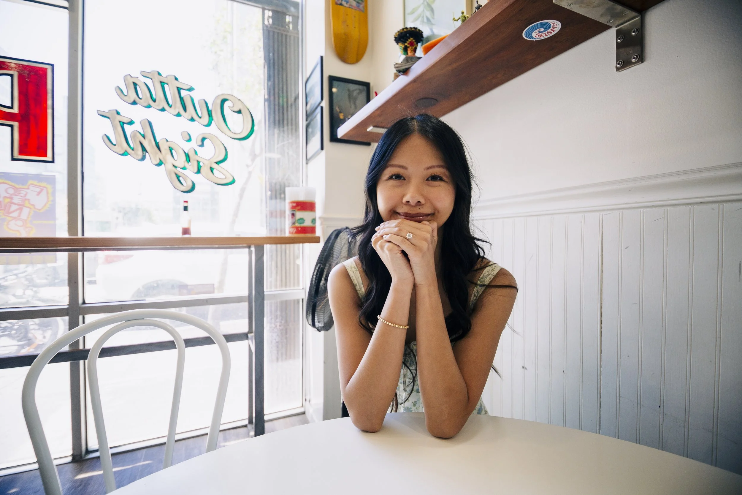Bride sitting on a table in a pizza shop with her hands under her chin looking toward the camera.