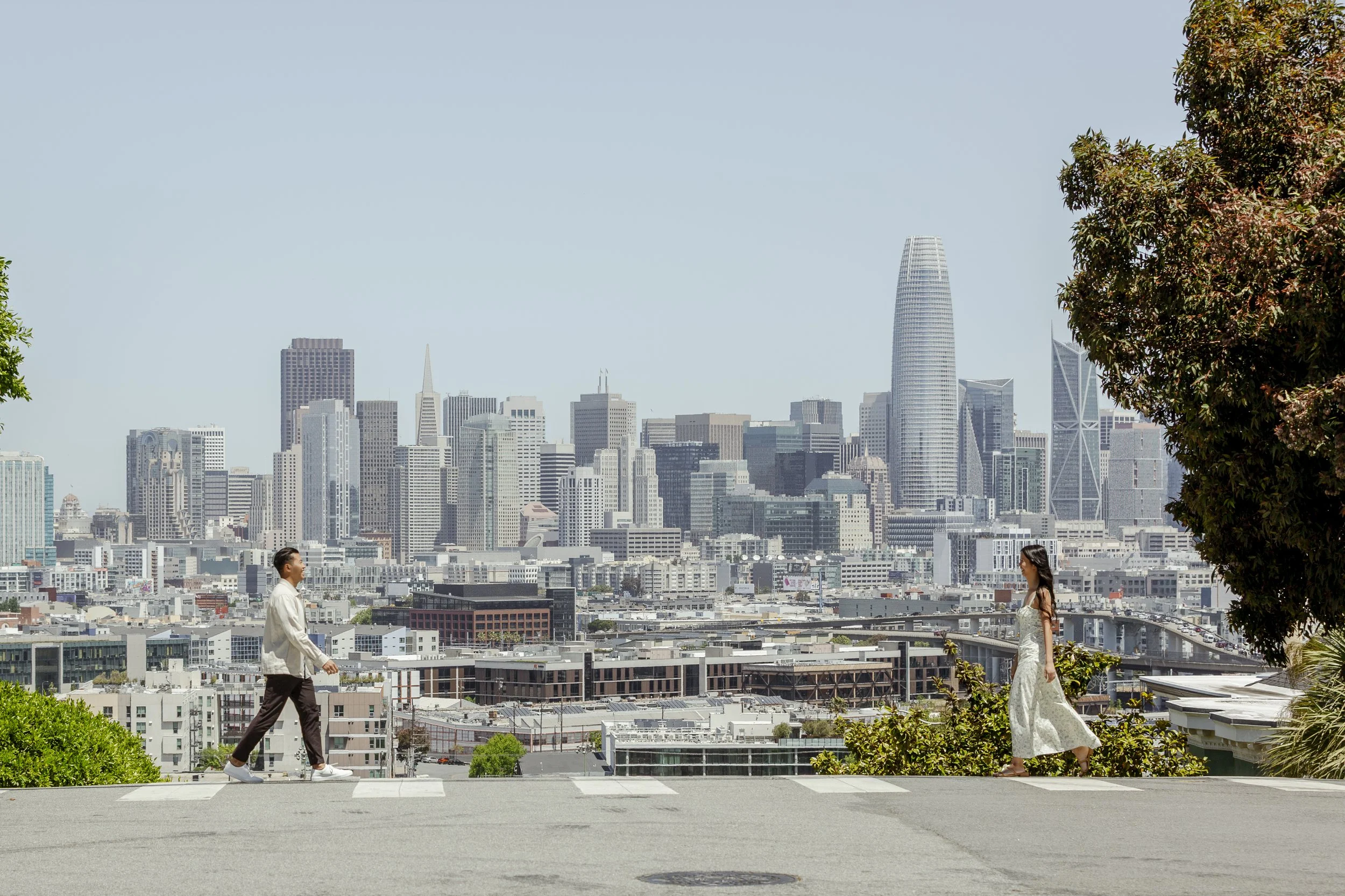 Couple crossing a street toward each other with the San Francisco skyline in the background during their engagement session.