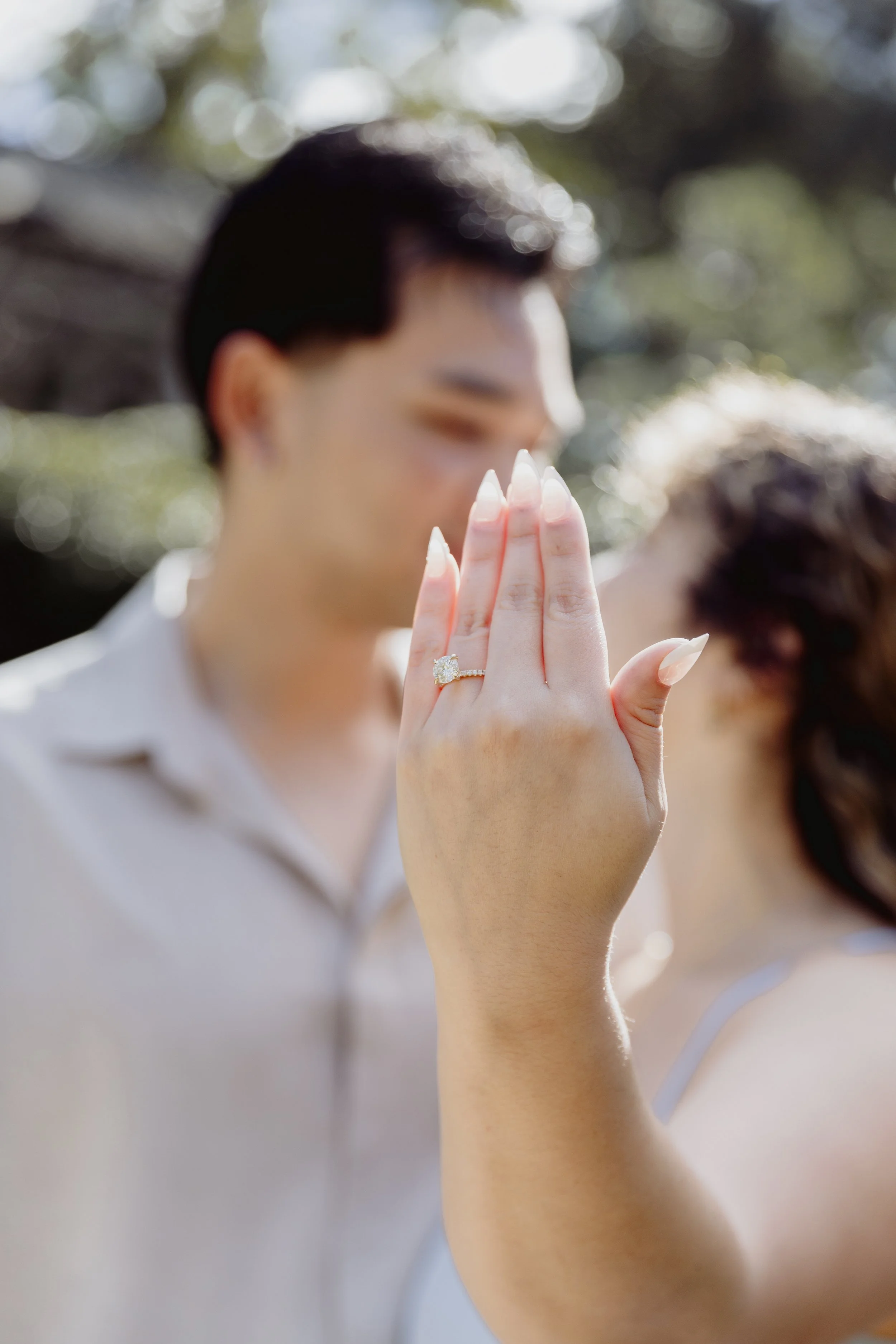 Engagement ring in focus with the couple softly blurred together in the background.