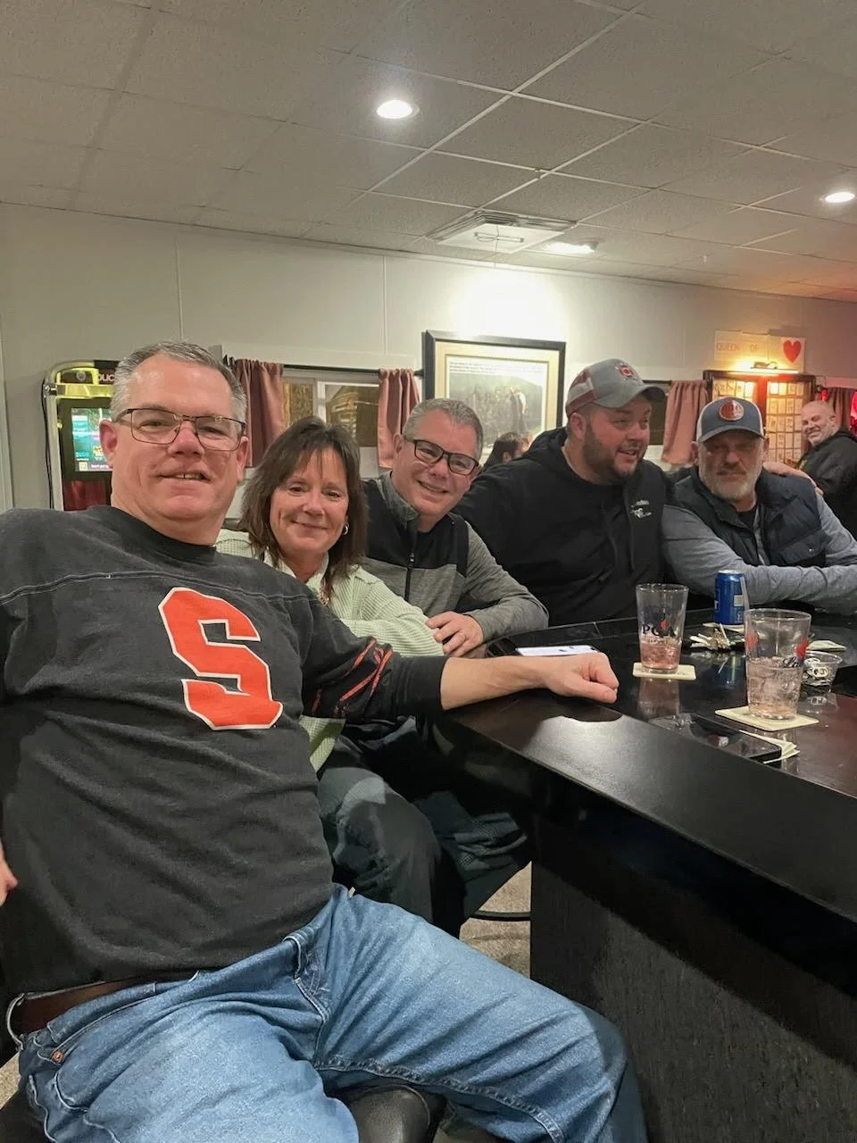 Group of five friends sitting at a bar table enjoying drinks and smiling.