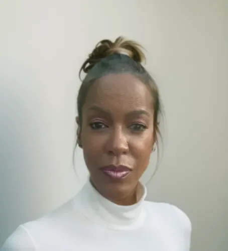 Portrait of a woman with styled hair wearing a white turtleneck against a plain background.