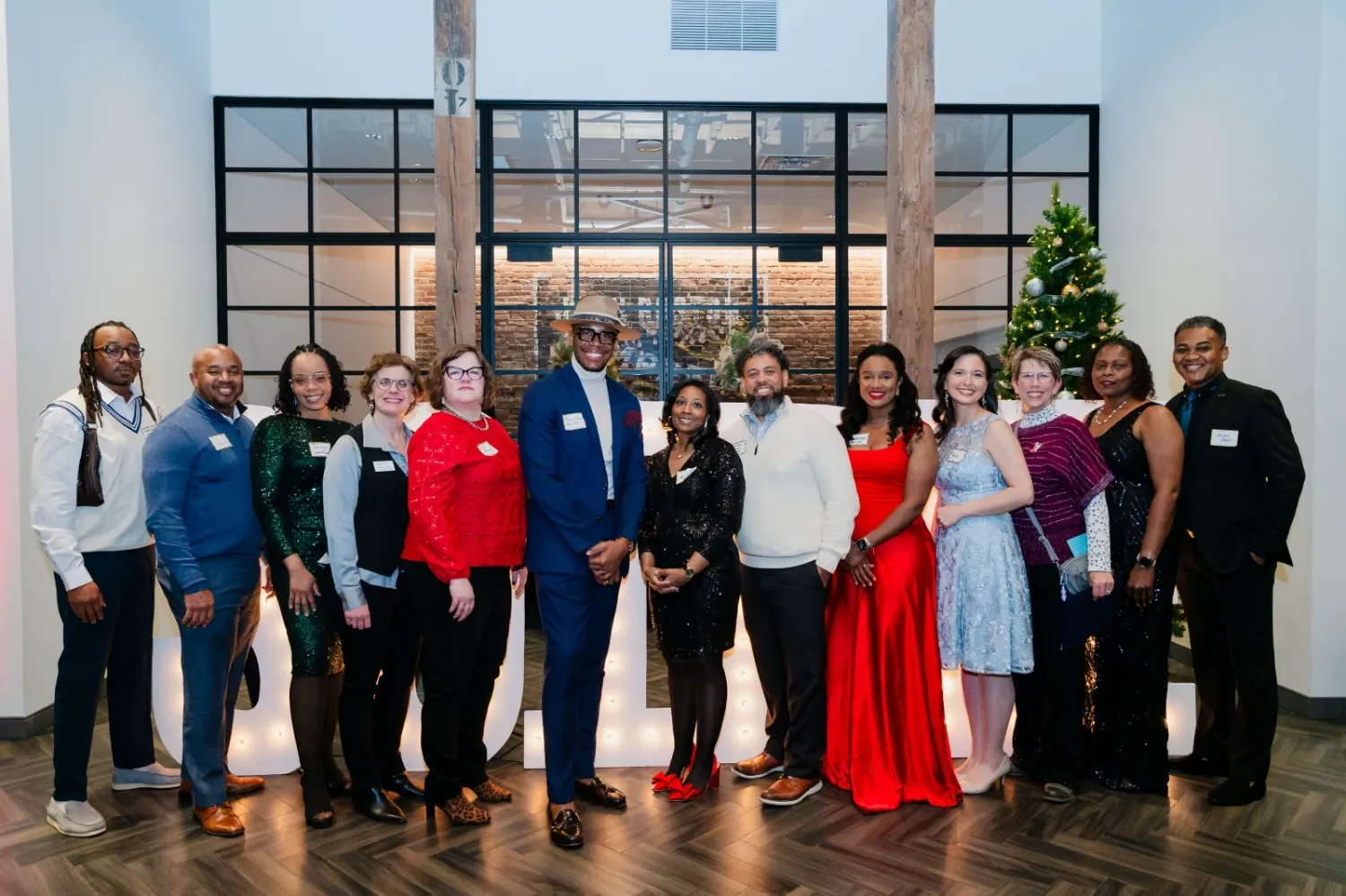 Group of diverse people dressed in formal and festive attire standing in front of a Christmas tree.
