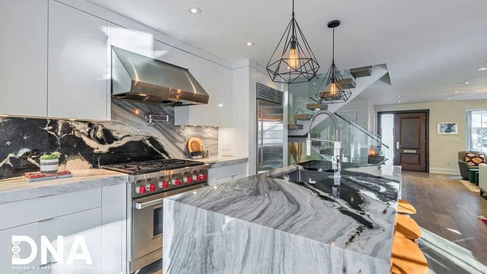 Modern kitchen with marble countertops, a stainless steel stove and oven, black and white marble backsplash, white cabinets, and decorative pendant lights.