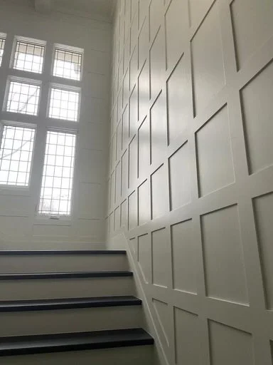 Interior of a stairway with a decorative wall and large windows letting in natural light.