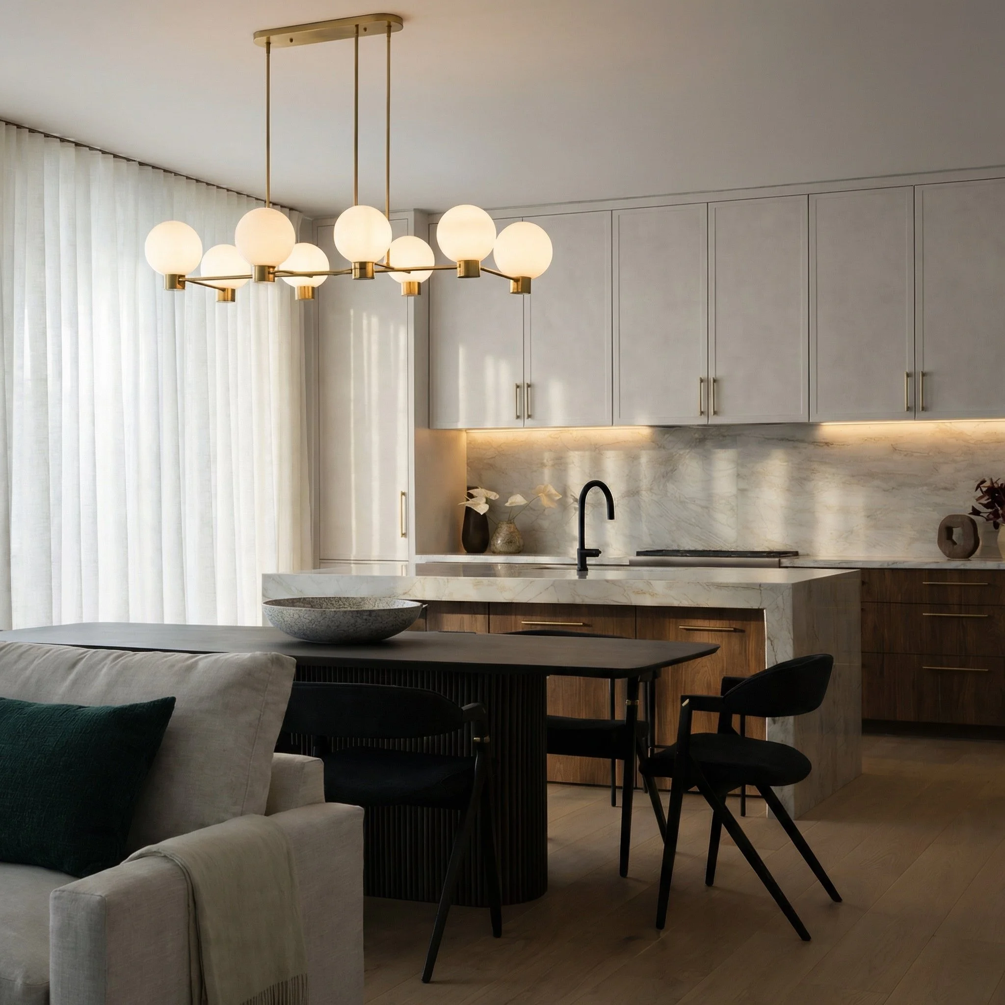 Modern kitchen and dining area with white cabinetry, marble backsplash, black faucet, black chairs, and a hanging light fixture with globe bulbs.