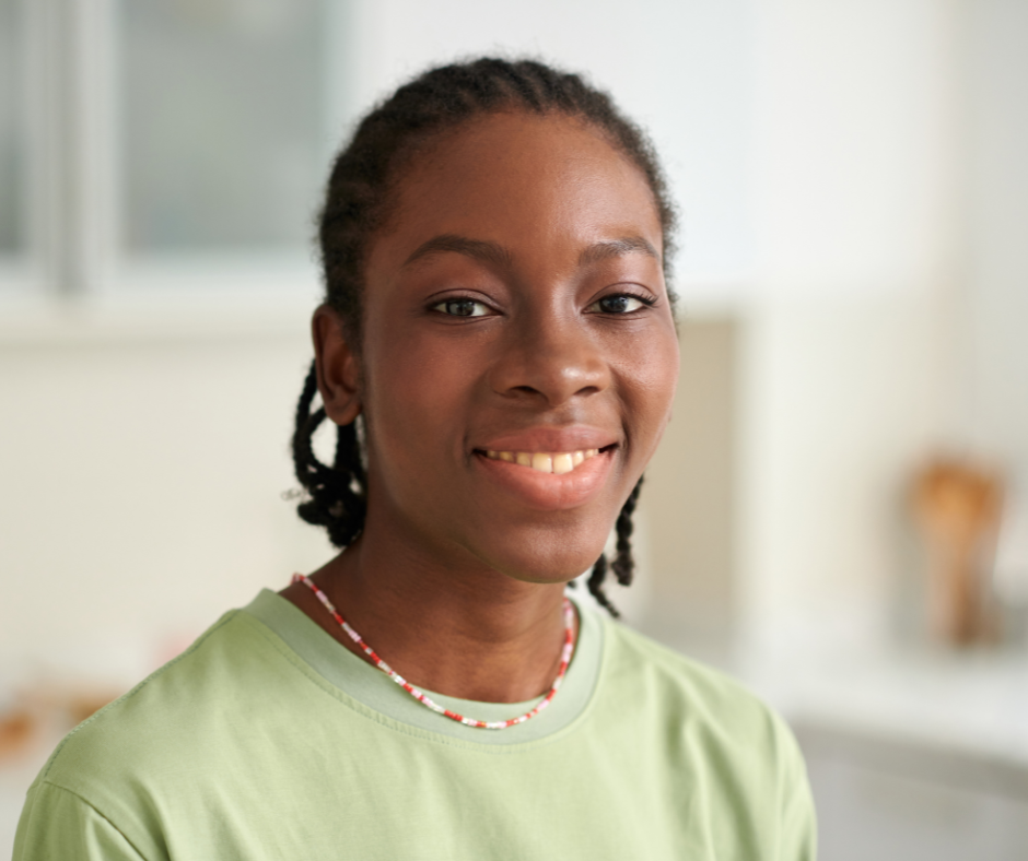 A young African American woman with braided hair, smiling in a light-colored kitchen.