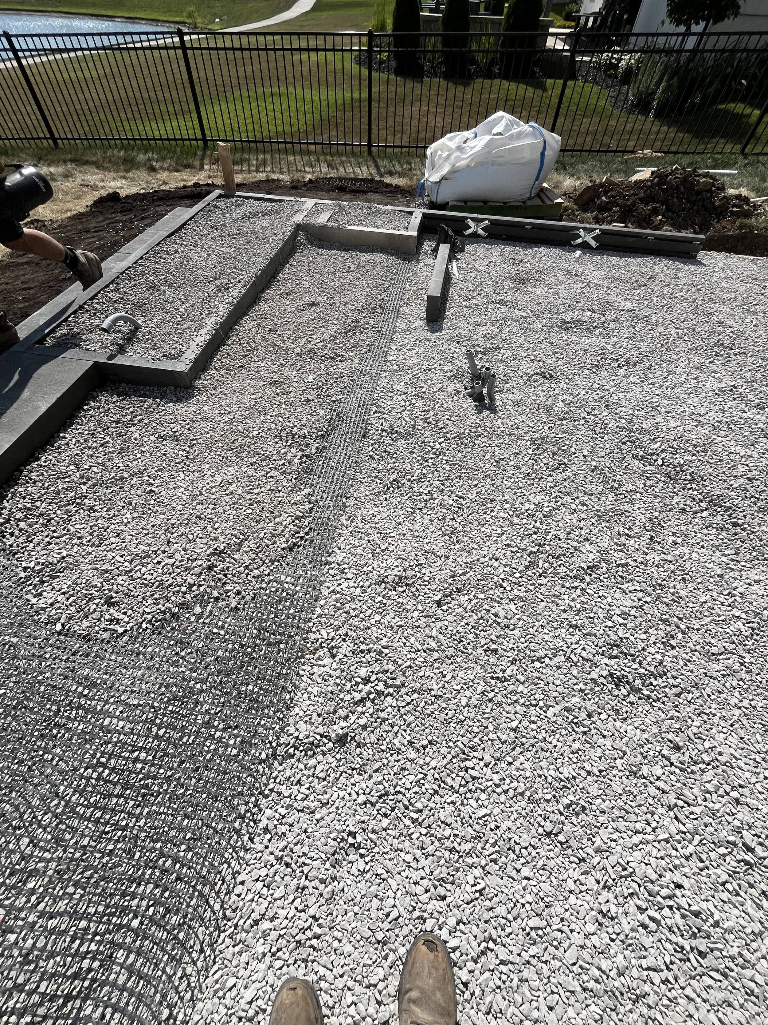 Construction site with gravel ground, metal framing, and tools, along with a white bag, missing the person's face.