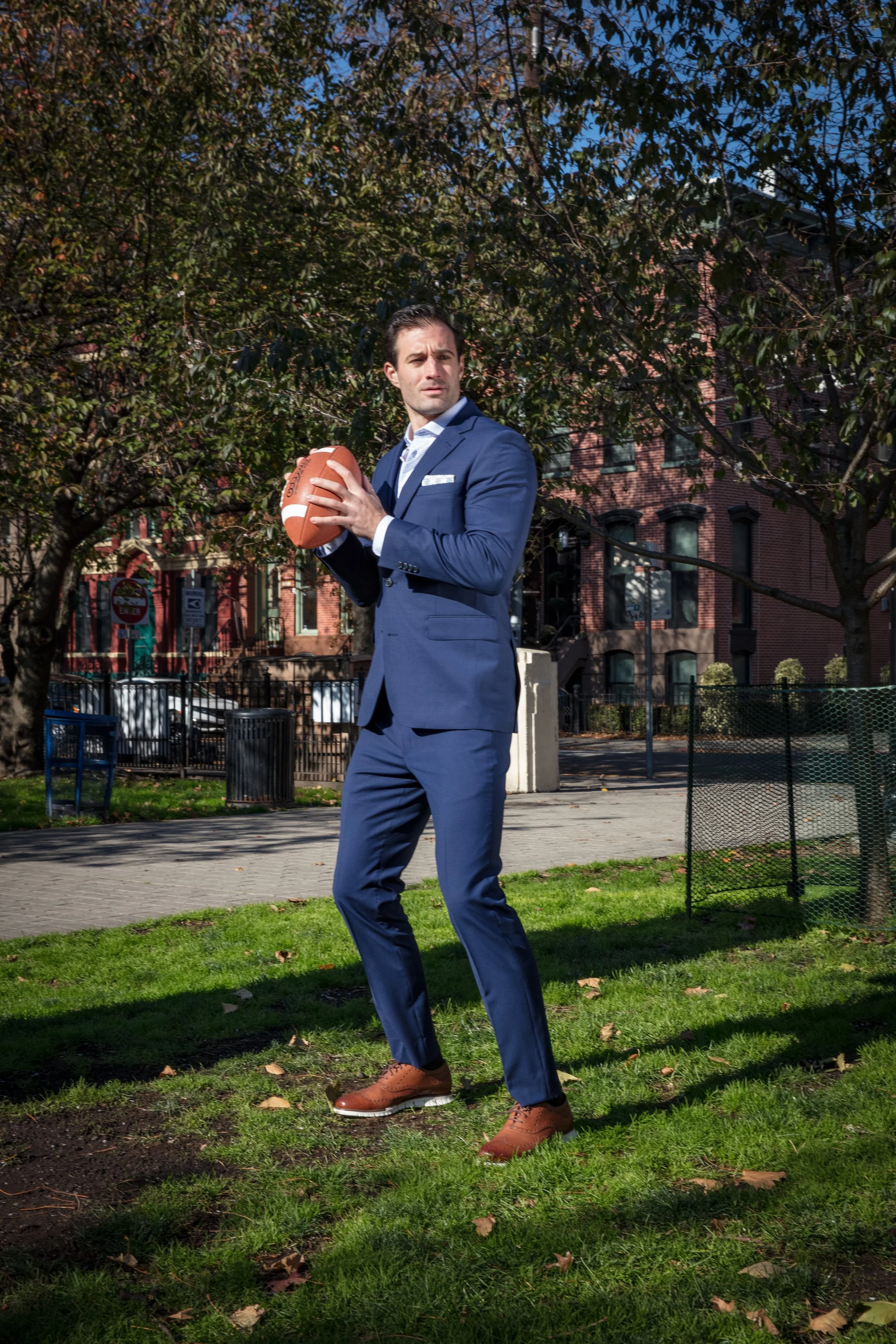 A man in a blue suit holding a football in an outdoor park setting.