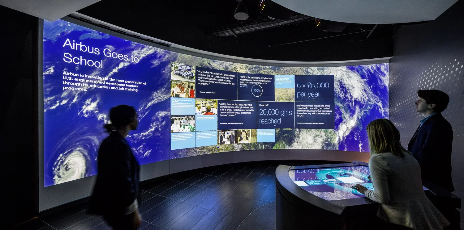 A sweeping 30-foot wall serves as a canvas for the host and visitors to intuitively explore featured stories. A rotating globe interface in the touchscreen table allows a multitude of project stories and data visualizations to be projected, and a hid