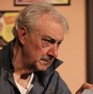 Close-up of an elderly man with gray hair looking downward, wearing a dark jacket.