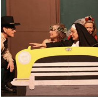 Four women dressed in costumes interacting with a yellow car prop.
