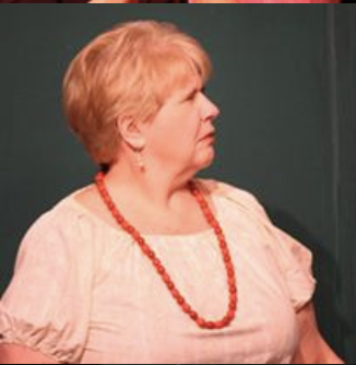 A woman with short, light-colored hair wearing a beige blouse and a red beaded necklace