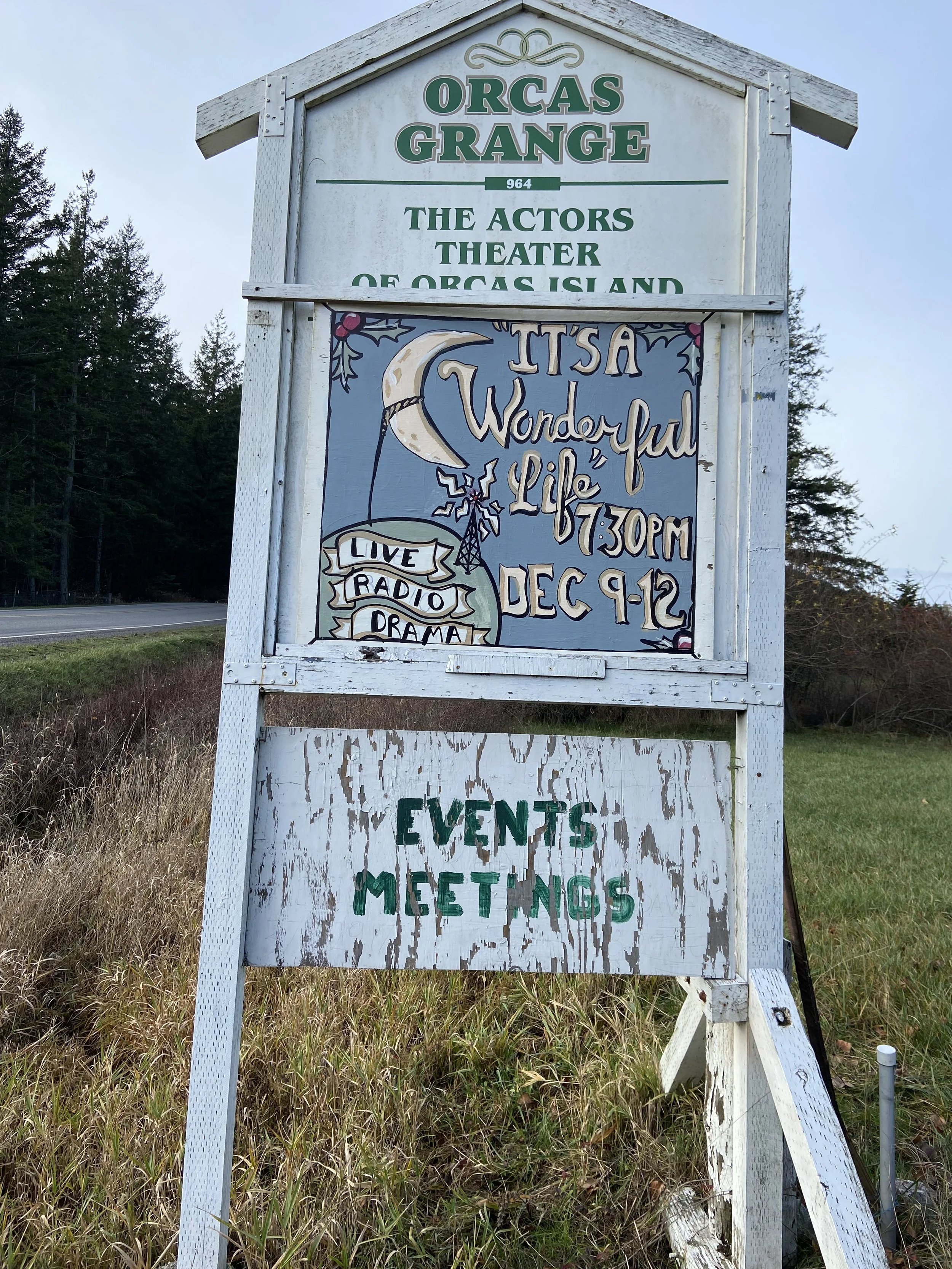 An outdoor sign for Orcas Grange, featuring information about a scheduled event called 'It's a Wonderful Life' on December 9-12, including performances at 7:30 PM with live radio drama. The lower part of the sign indicates 'Events' and 'Meetings'.